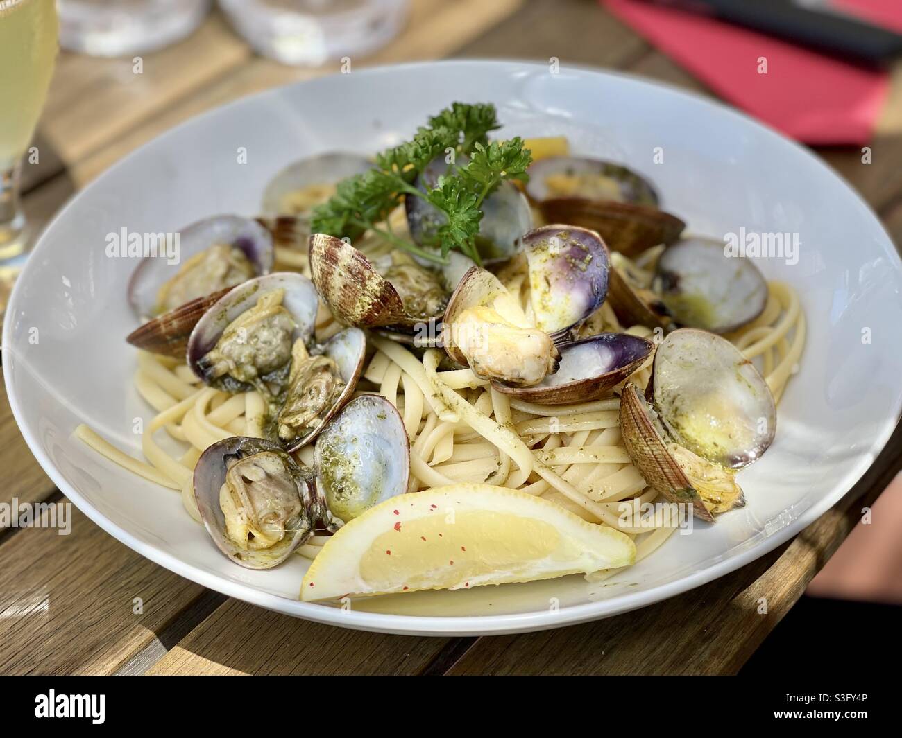 Seafood pasta plate with clams, lemon and parsley on a white restaurant table in an Italian restaurant in the south of France - Smartphone Captured Stock Image