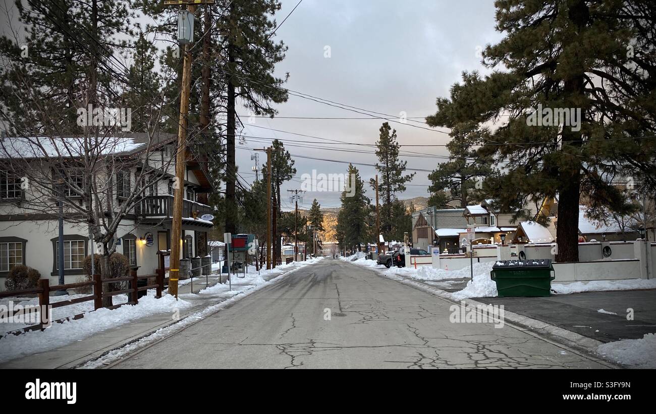 Big Bear, CA, Dec 2020: view along street with overhead telephone lines and power cables, pine trees and snow at sides, mountains in distance and overcast skies Stock Photo