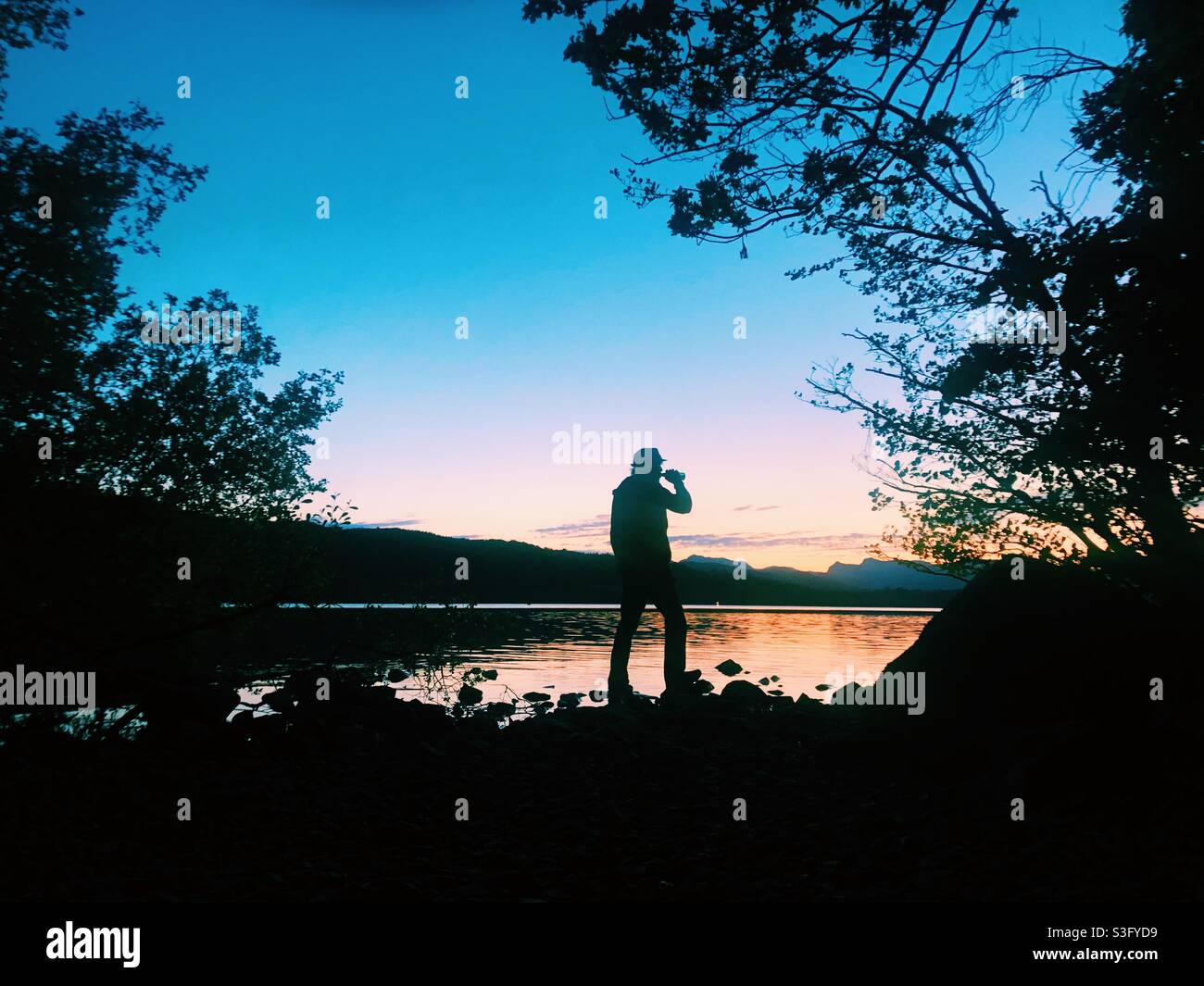 Man drinking a beer watching the sunset over lake Windermere - Smartphone Captured Stock Image