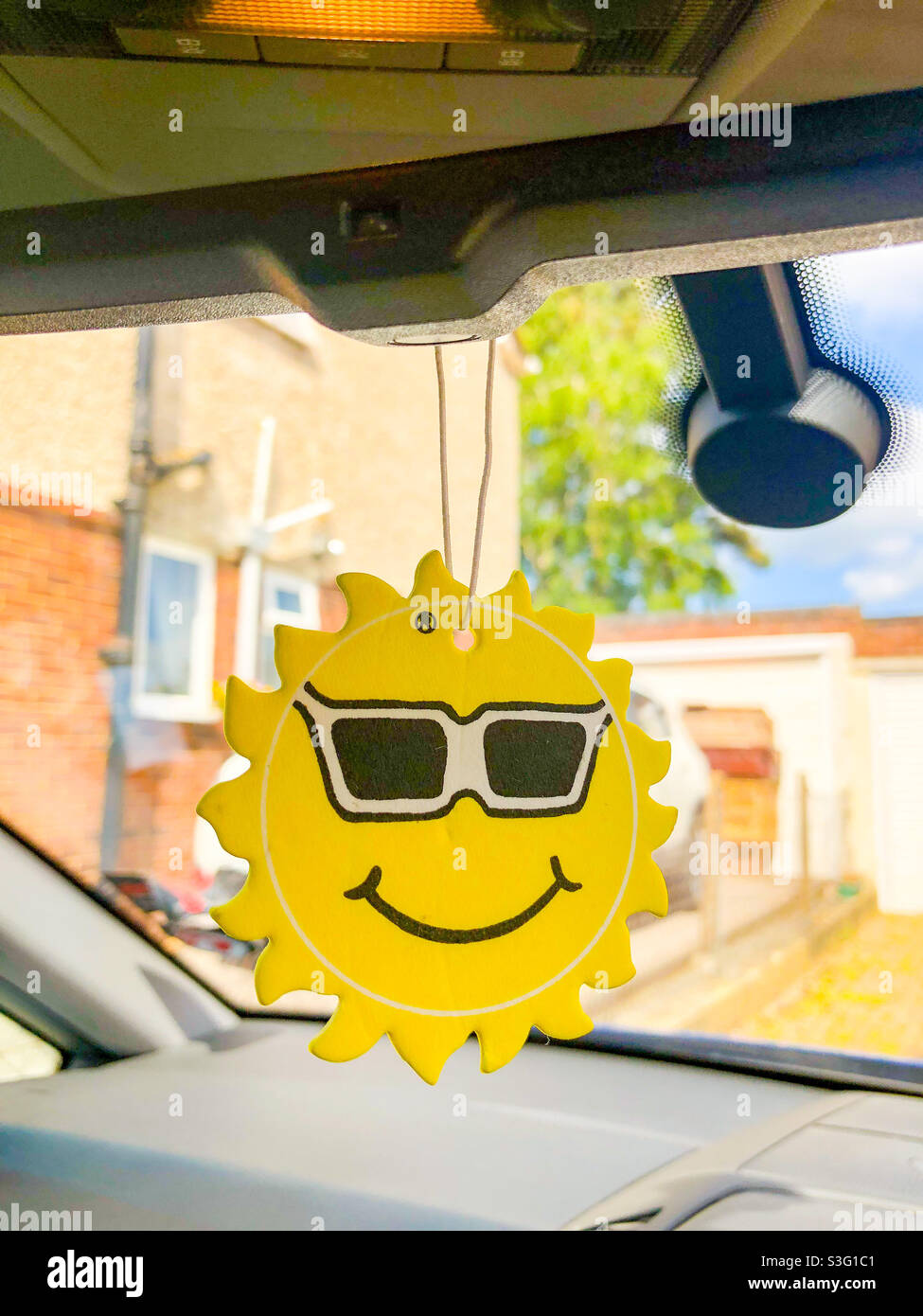 A car air freshener in the form of a smiling sun wearing sunglasses. - Smartphone Captured Stock Image