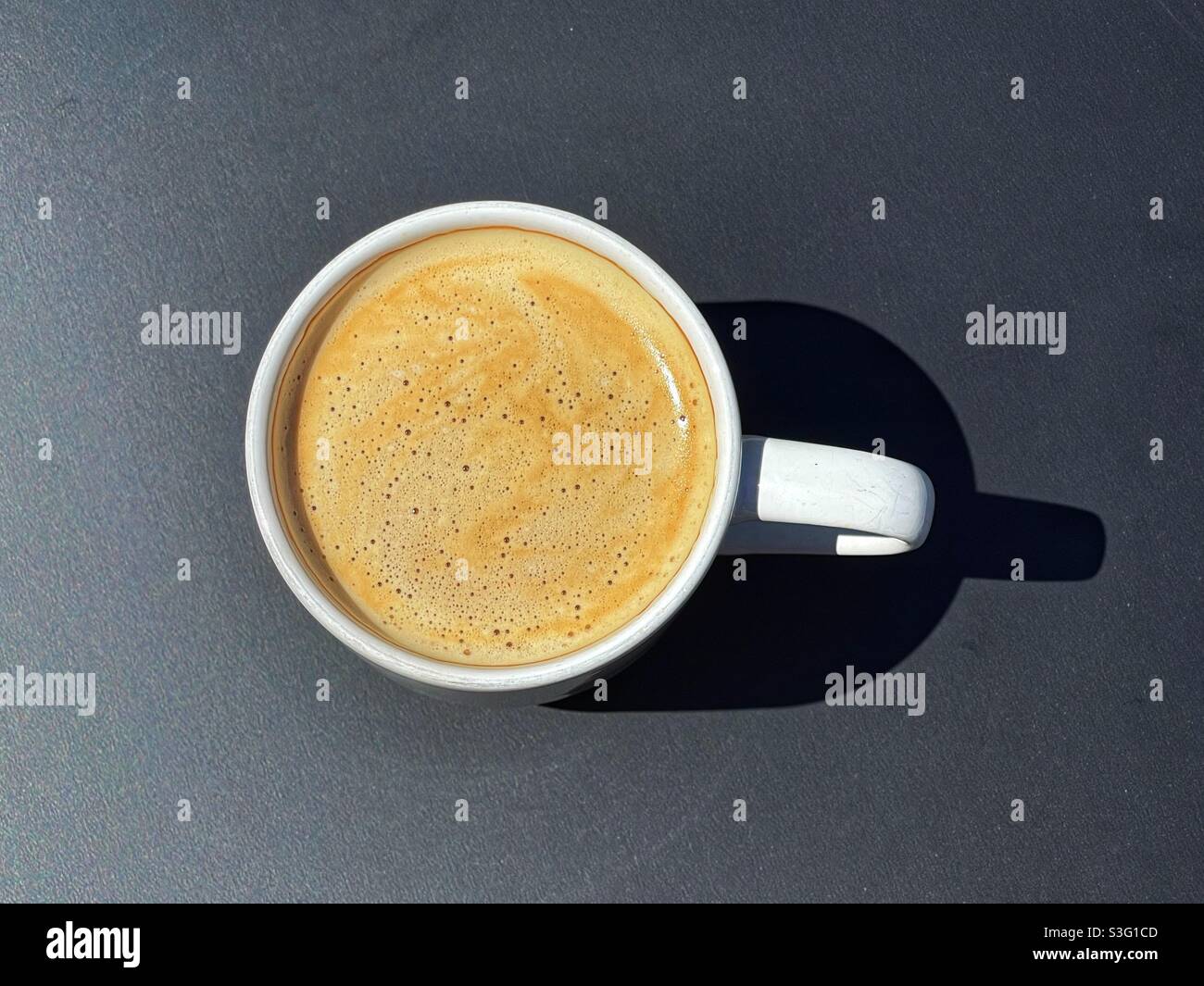 Overhead closeup view of a cup of fresh coffee in a white cup on a black tabletop - Smartphone Captured Stock Image