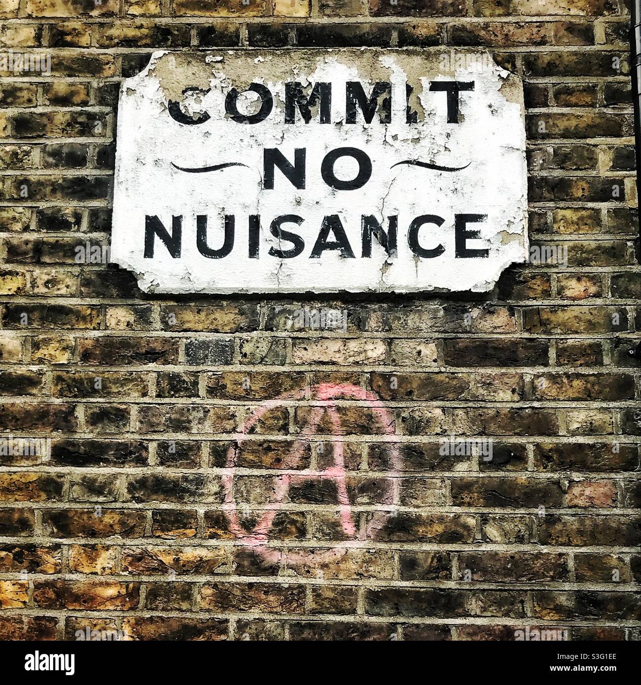 Old sign on wall in south London reading ‘Commit No Nuisance’ underneath is a graffitied anarchy sign - Smartphone Captured Stock Image
