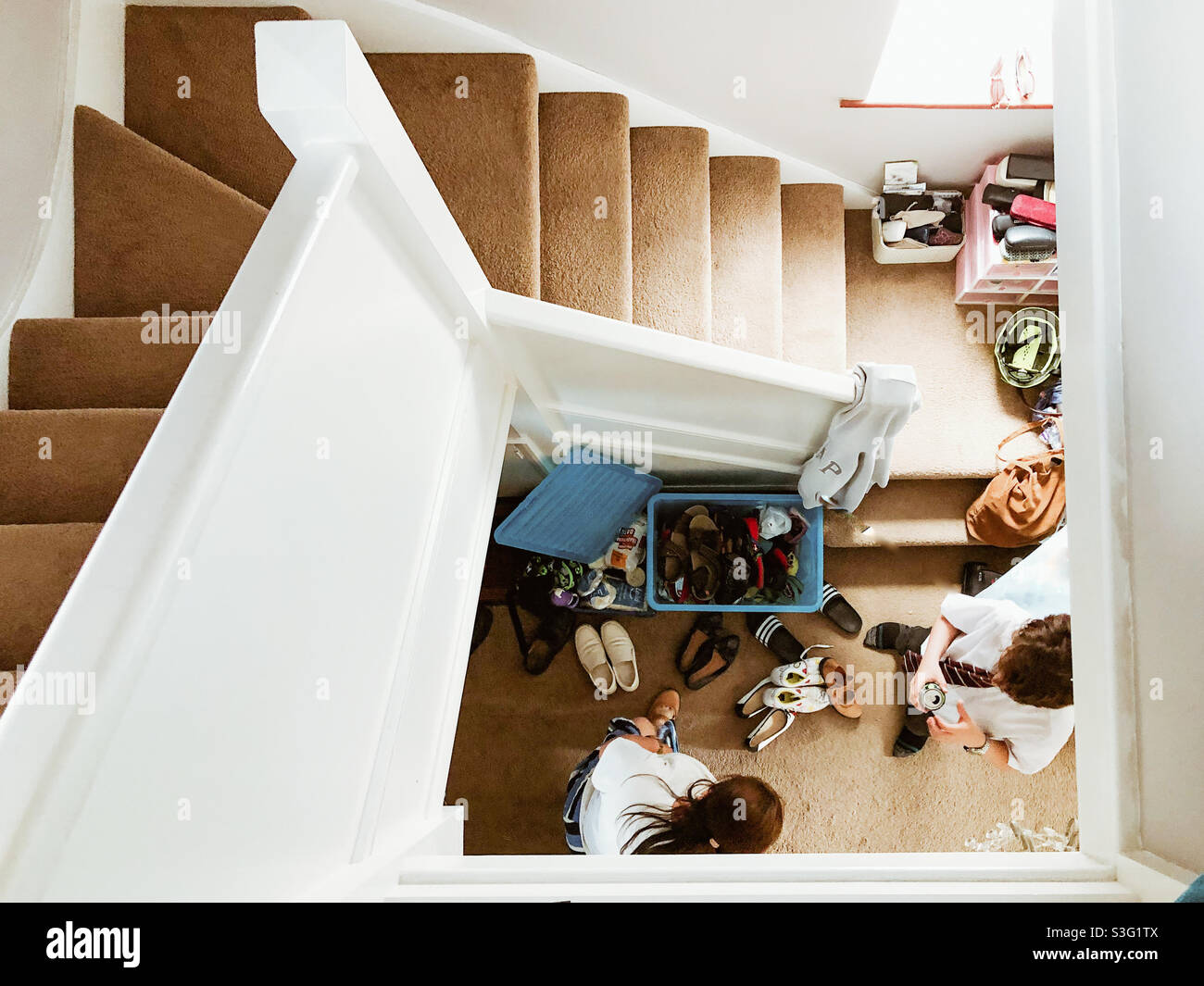 Looking down a staircase at people sorting a box of shoes in the hallway below. - Smartphone Captured Stock Image