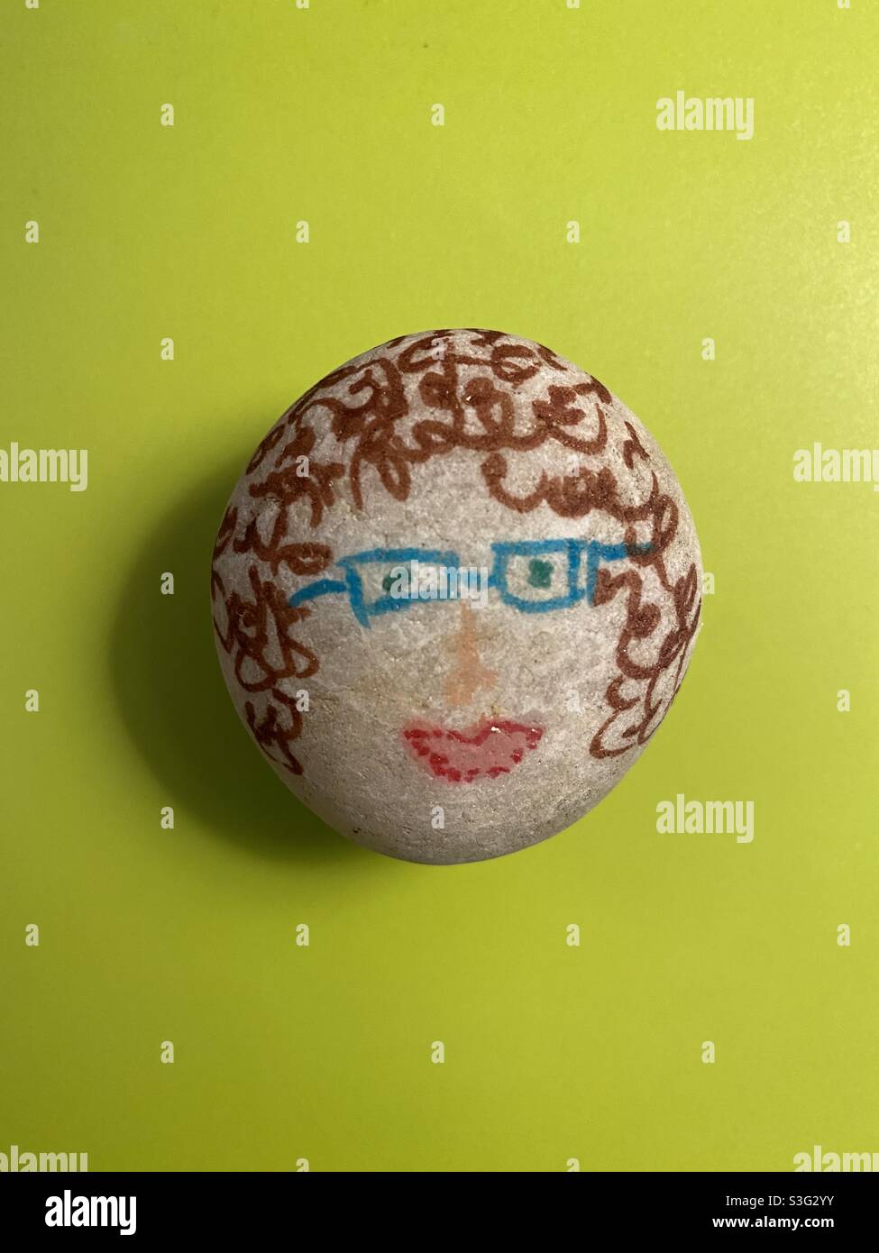 Rock painted to be a smiling woman wearing blue glasses and curly hair. - Smartphone Captured Stock Image