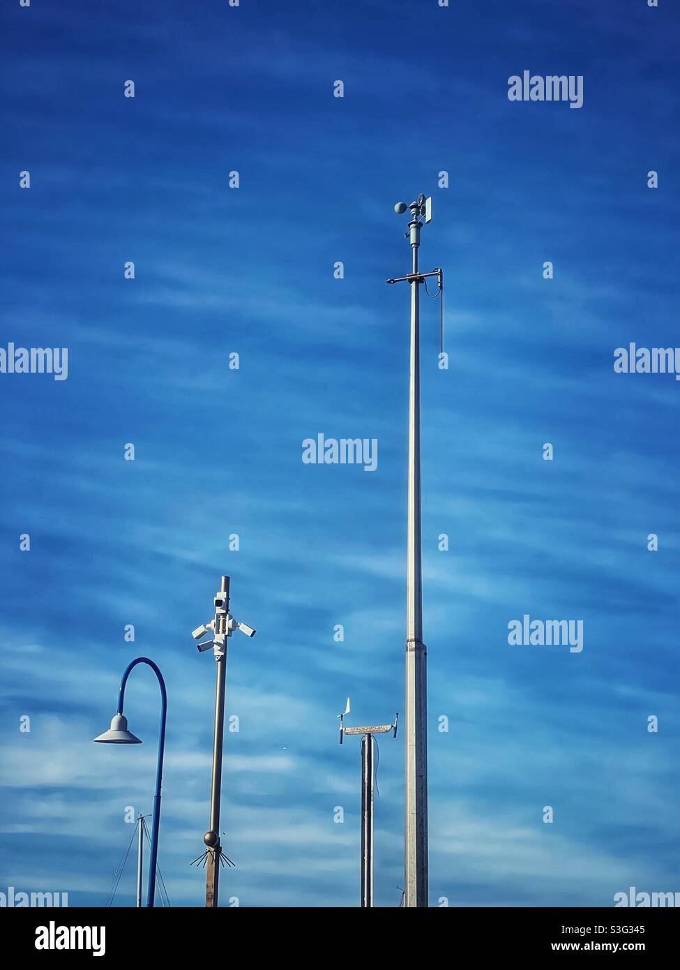 Weather station, surveillance cameras and overhead lighting against blue sky and streaky clouds - Smartphone Captured Stock Image