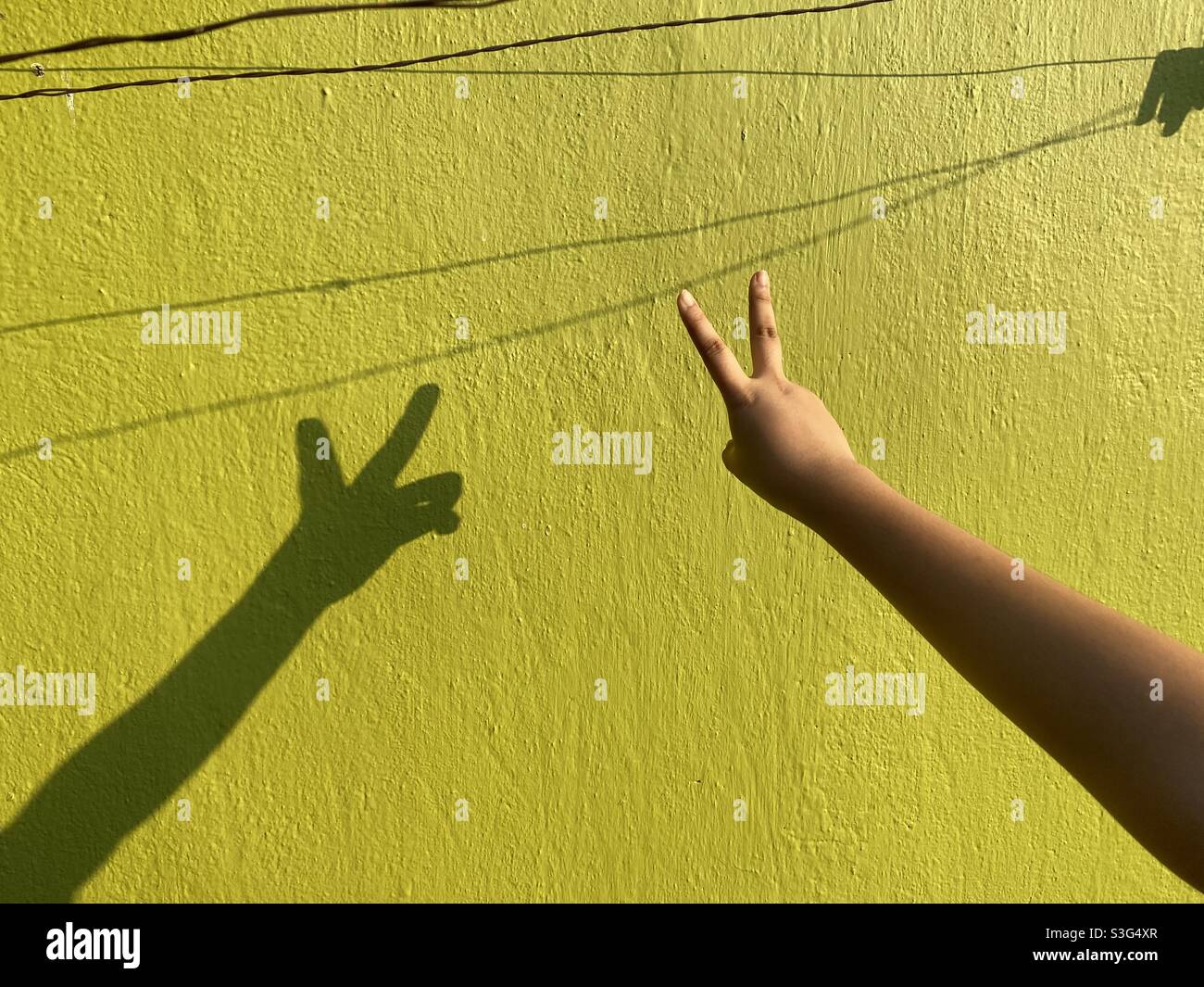 A girl showing V sign for victory against a cemented wall - Smartphone Captured Stock Image