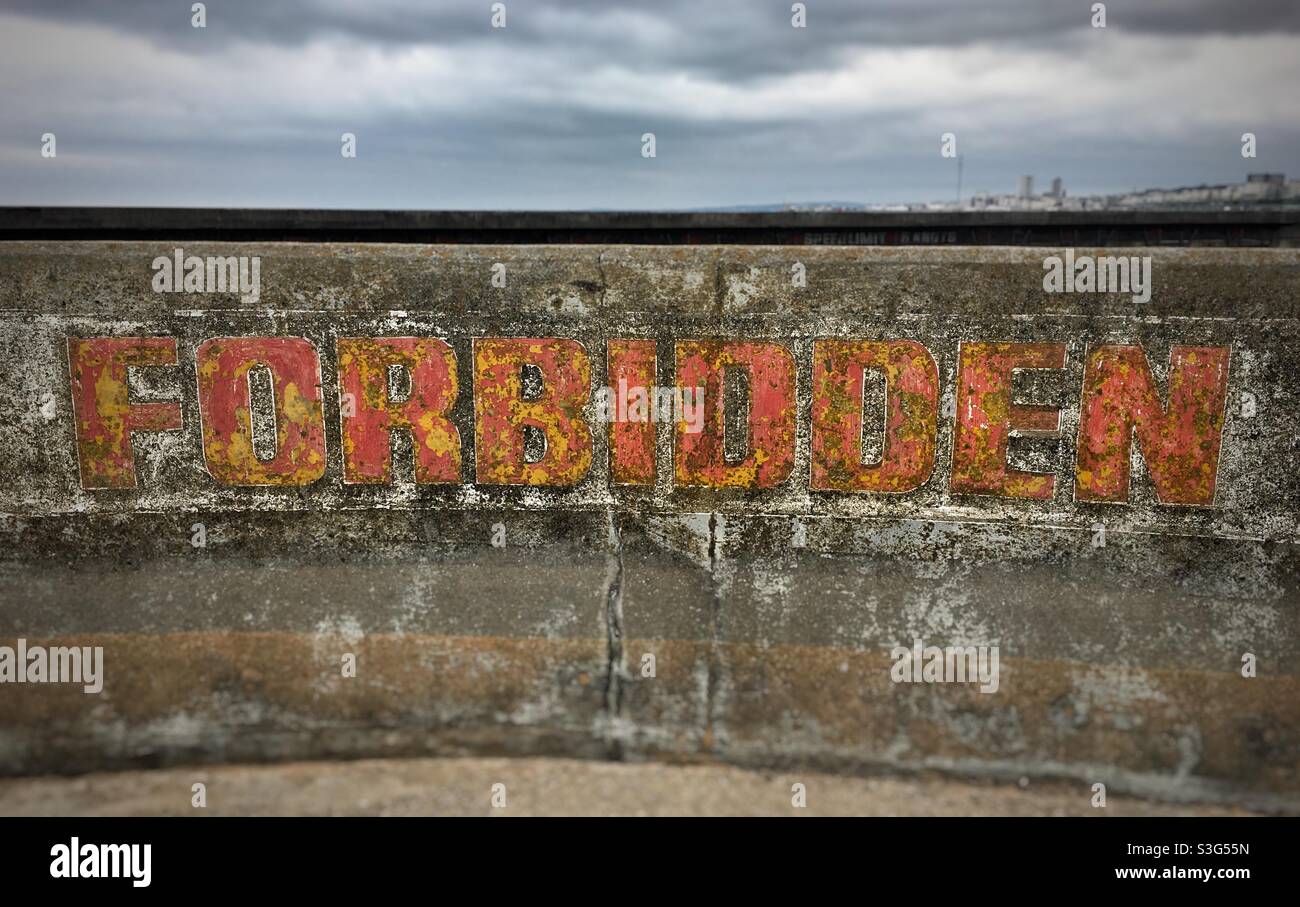 The word “Forbidden” written in flaking orangey red paint on a concrete wall - Smartphone Captured Stock Image
