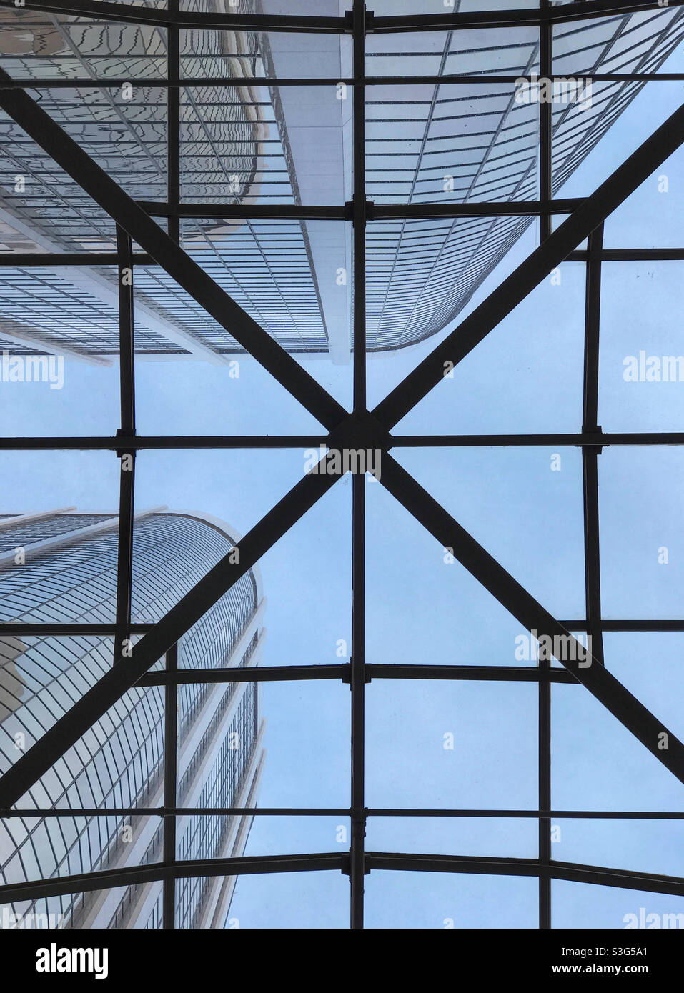 Looking up through the patterned glass ceiling, to the towering office buildings and the blue sky beyond. Downtown in the city of Calgary, Alberta, Canada. - Smartphone Captured Stock Image