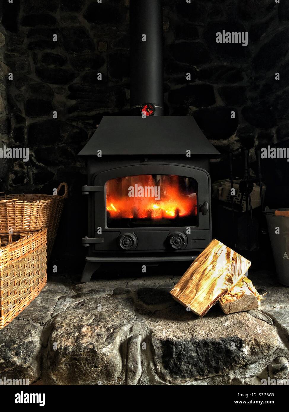 Cozy stone cottage home interior with a fire blazing in a wood burning stove fireplace Stock Photo