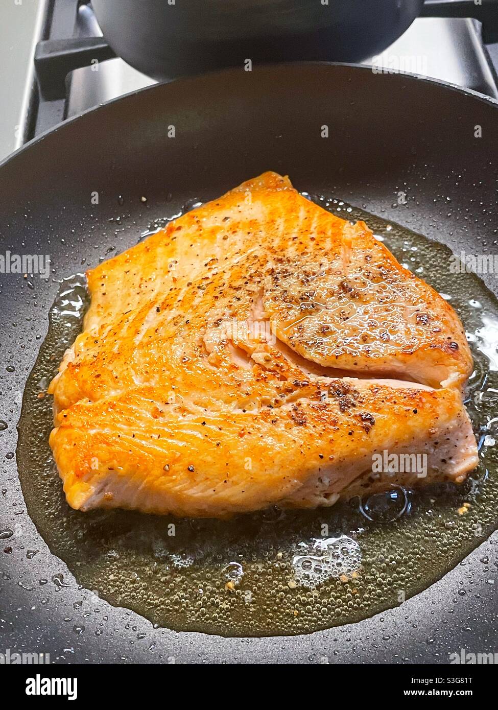 Fresh salmon fillet sautéing in A skillet on a residential stove top, USA - Smartphone Captured Stock Image