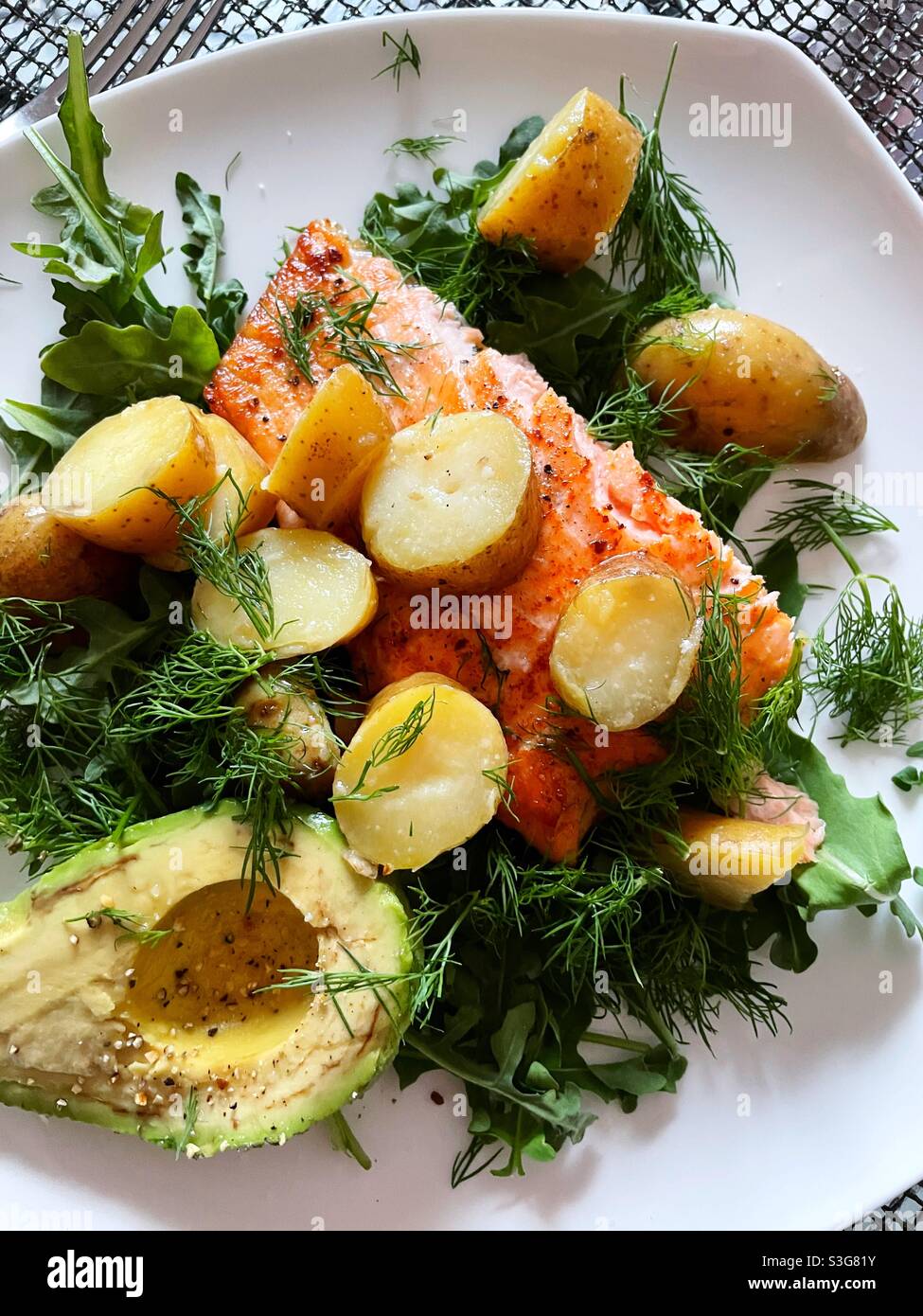 Flat lay of a seared salmon fillet on a bed of arugula with sliced creamery new potatoes and half an avocado and a spicy vinaigrette - Smartphone Captured Stock Image