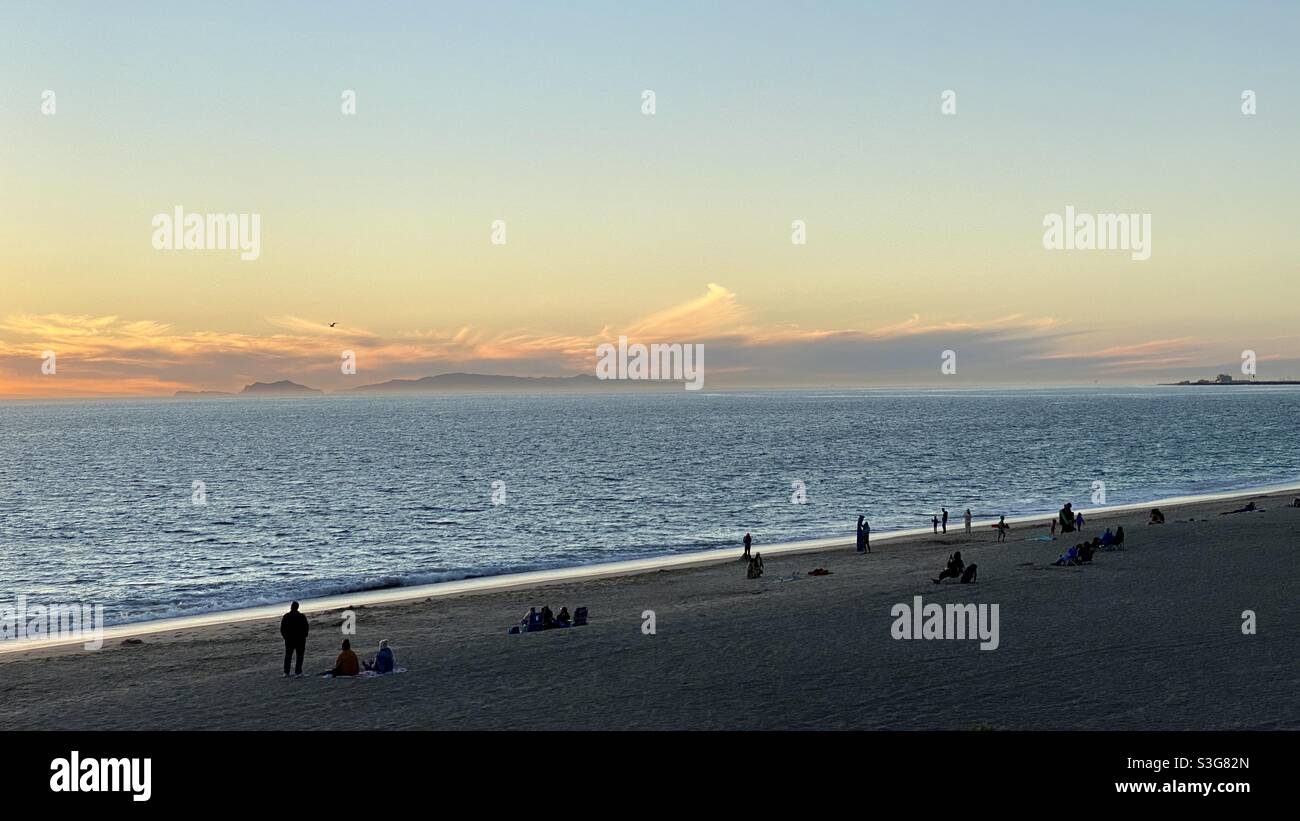 Silhouetted people on beach at Point Mugu, California, with sun setting over the Pacific Ocean. Catalina Island visible on the horizon - Smartphone Captured Stock Image