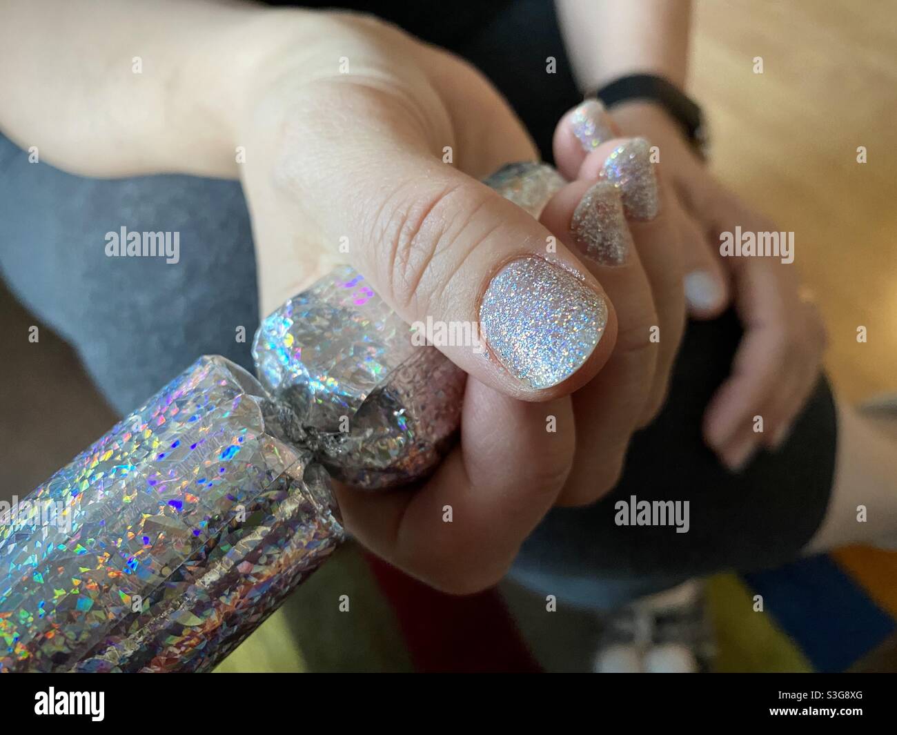 Woman's hand with glitter nail polish grasps a glittery Christmas cracker as she pulls it with someone out of frame - Smartphone Captured Stock Image