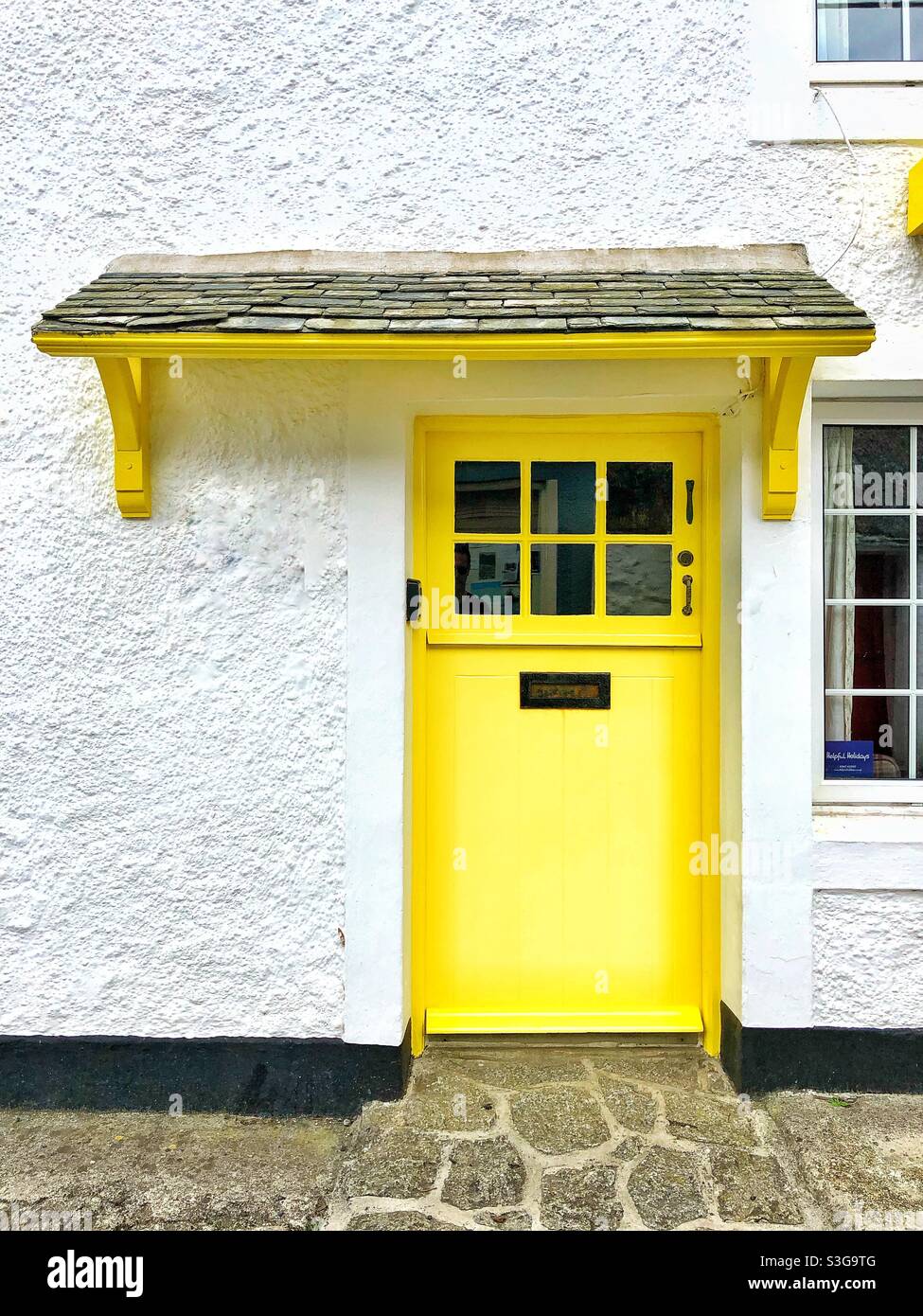 A bright yellow front door with overhead canopy in a stone whitewashed cottage Stock Photo