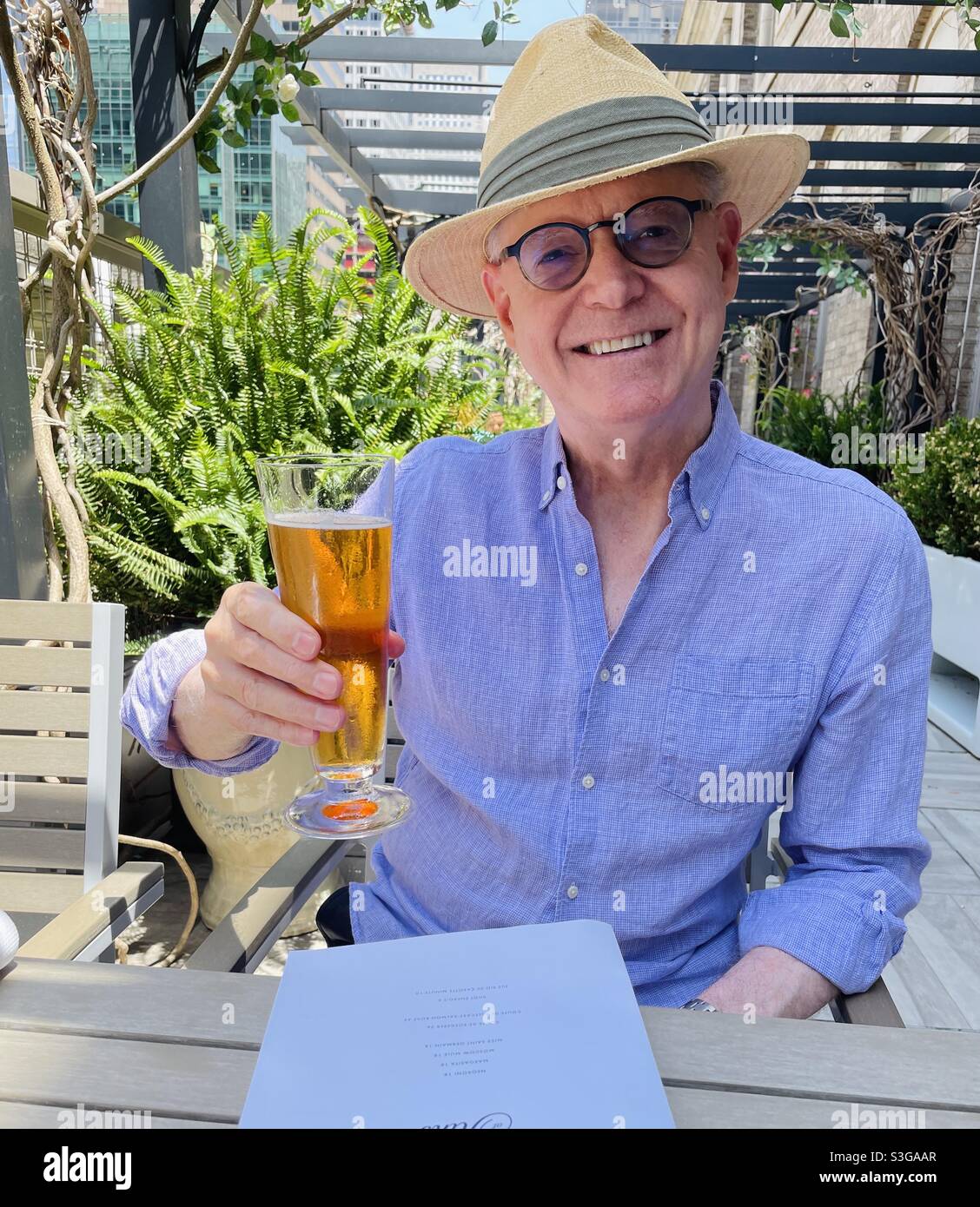 Handsome and happy senior man enjoying a beer at an outside rooftop terrace in Midtown Manhattan on a Summer Day, NYC, USA - Smartphone Captured Stock Image