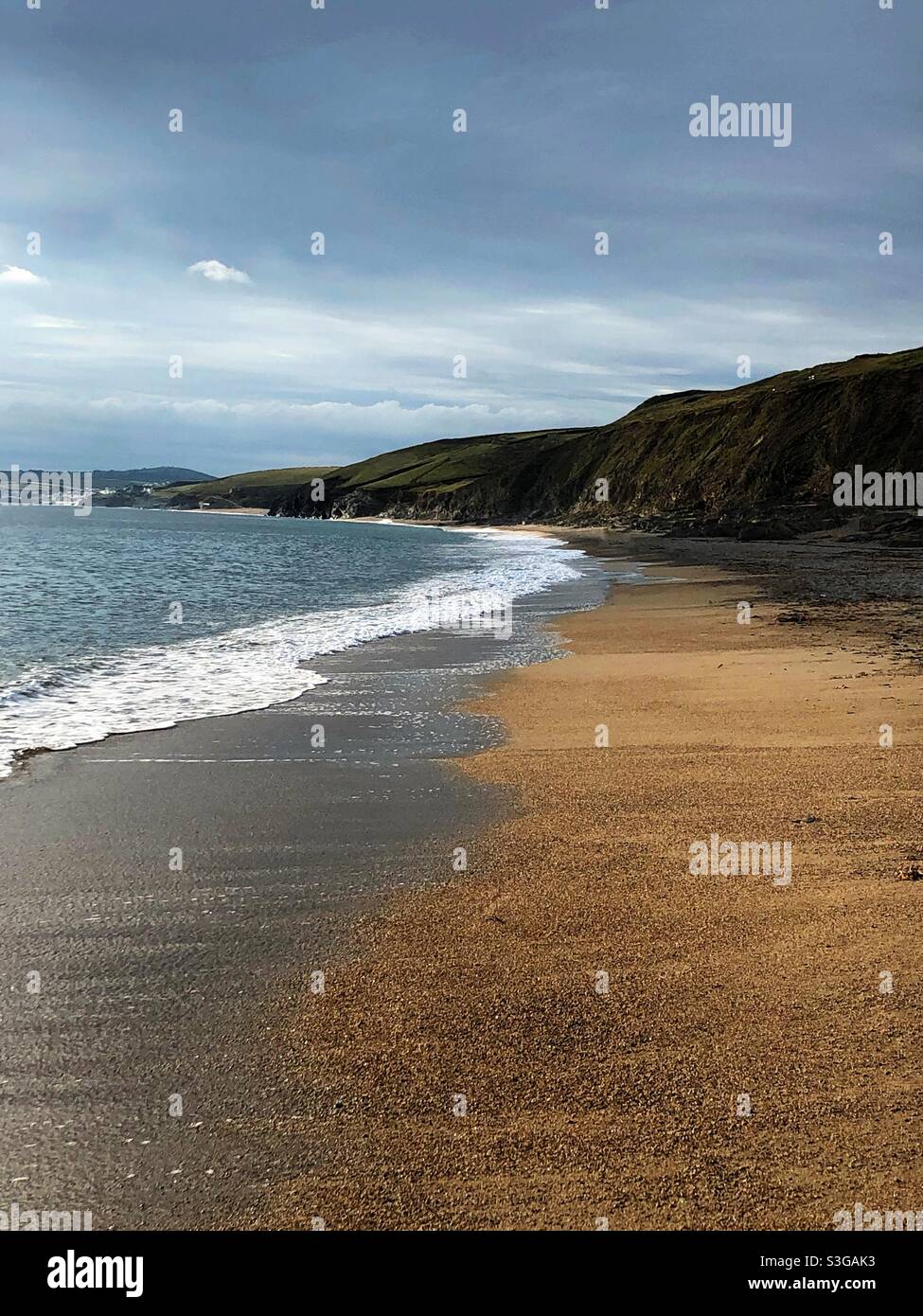 A deserted red sandy beach in Gunwalloe, Cornwall with white waves washing surf up - Smartphone Captured Stock Image