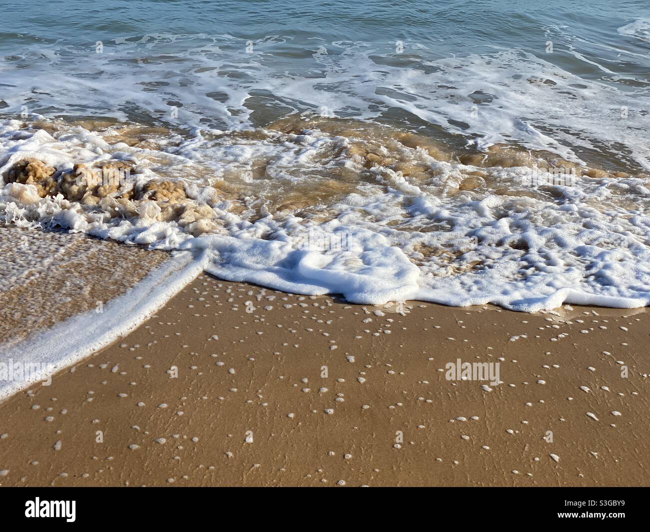 Foamy sea water lapping a sandy beach Stock Photo