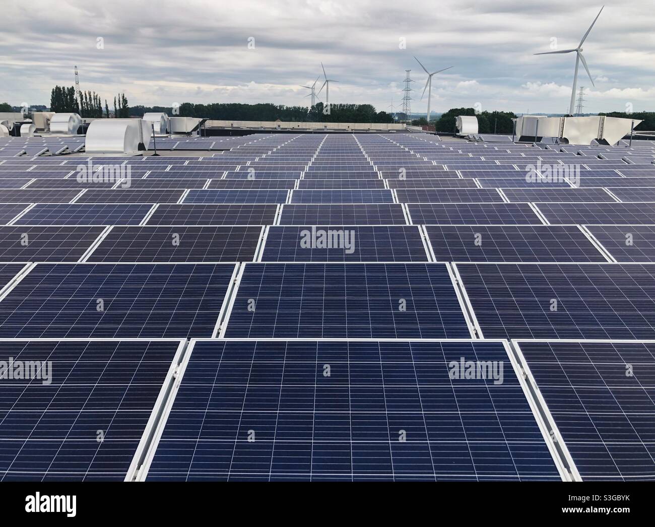 Rooftop with rows of solar panels and wind turbines in the background ...
