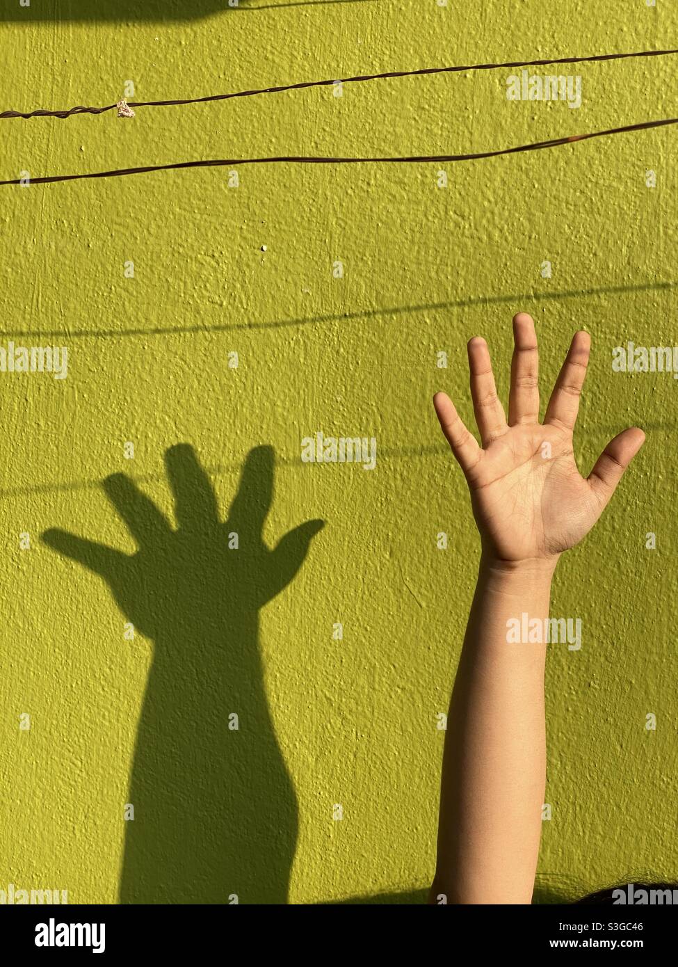 A teenage girl raising her hand against a cemented wall Stock Photo