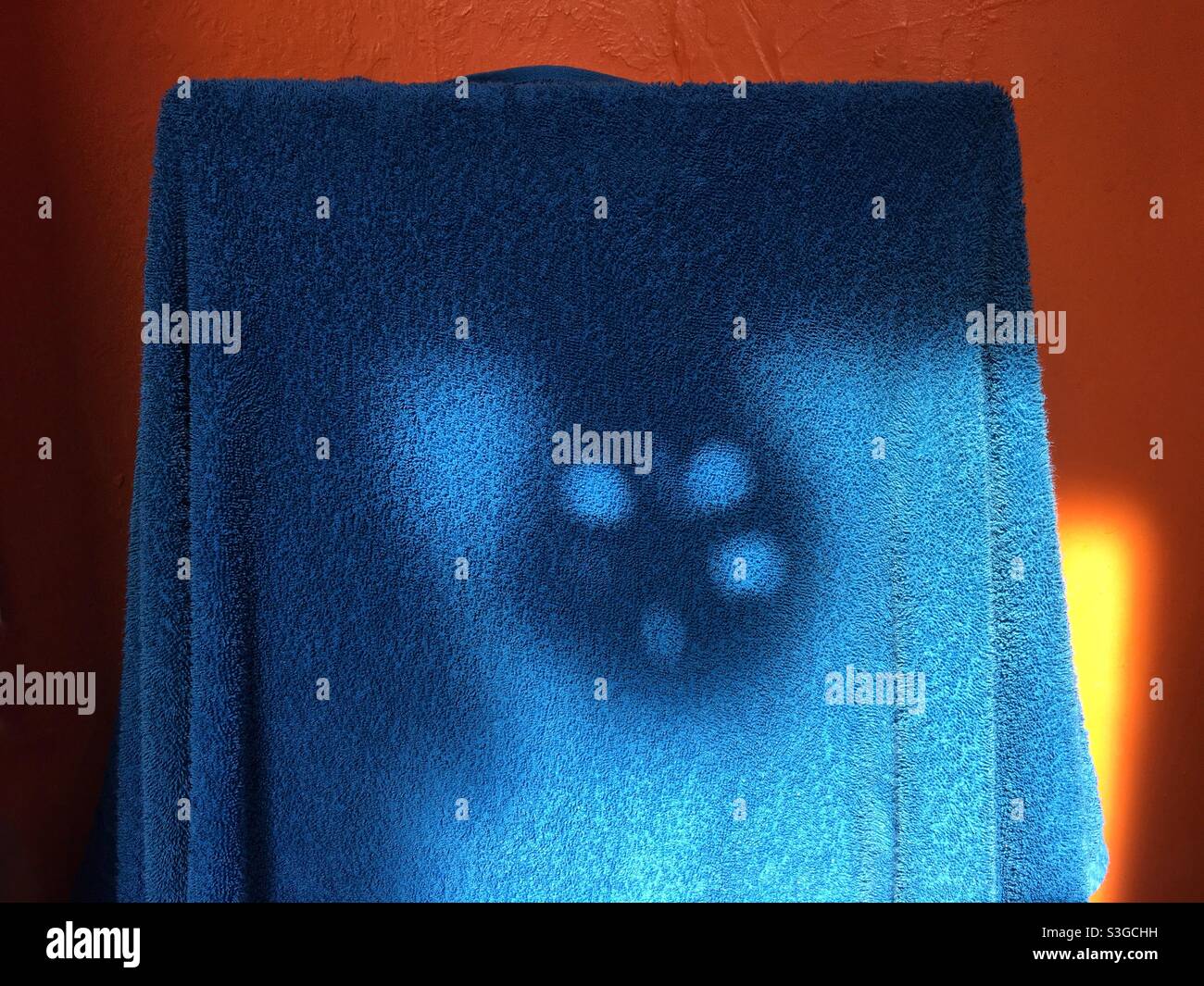 Mysterious shadow on a blue towel in front of an orange wall - Smartphone Captured Stock Image