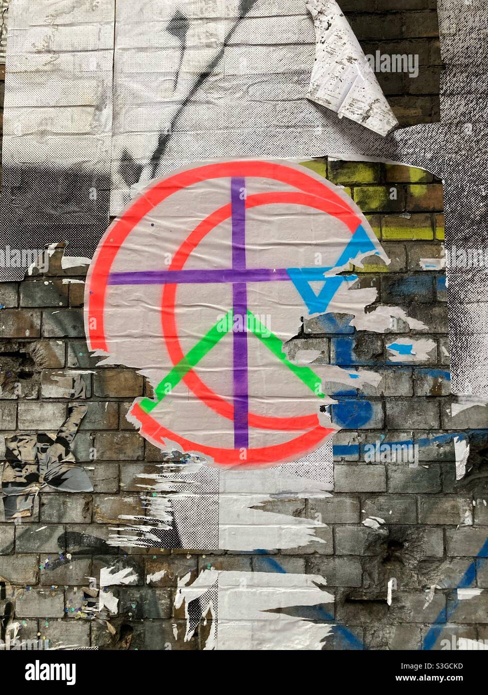A Poster on a Wall showing combined popular symbols: Peace, cross, Star of David; partly ripped of Stock Photo