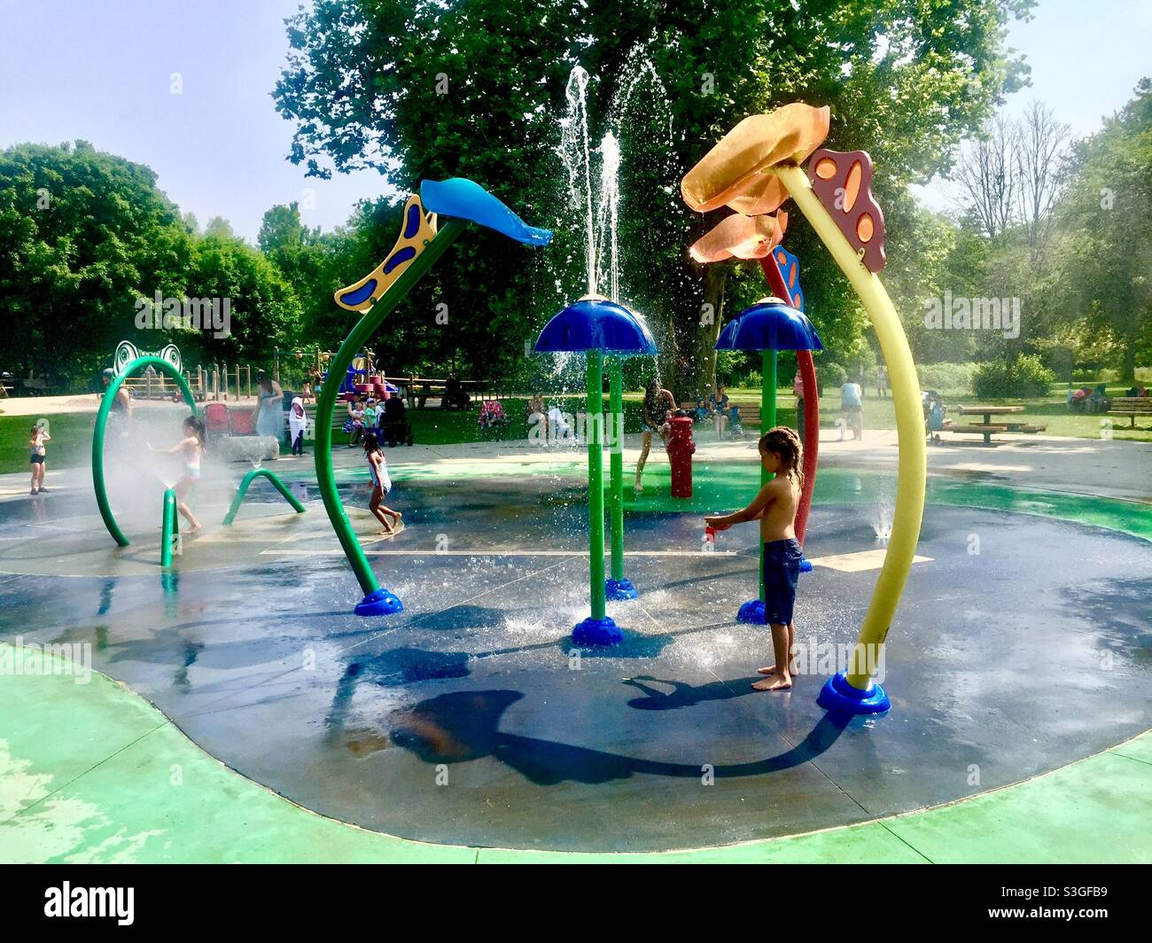 Gentle, summer,  fun. Kids in a modern splash pad in an outdoor setting. Cascading, splashing, spraying, water in a lovely park, Ontario,Canada. - Smartphone Captured Stock Image