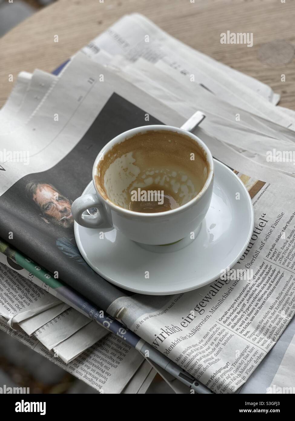 End of morning routine with an empty cappuccino cup over newspapers on a bar table - Smartphone Captured Stock Image