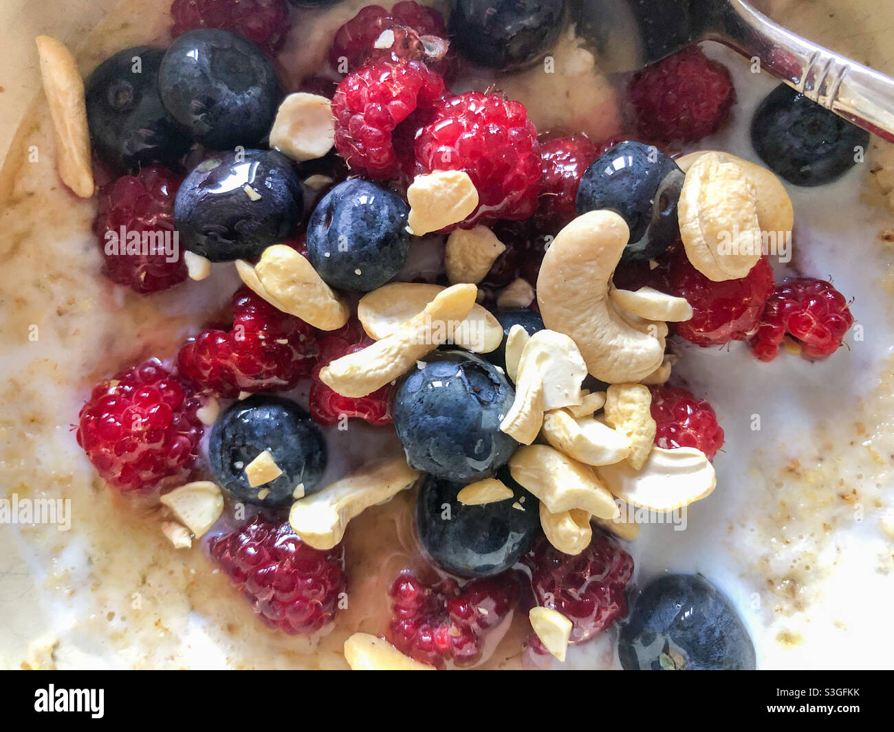 Close up view of porridge with raspberries, blueberries and cashew nuts for breakfast. Stock Photo