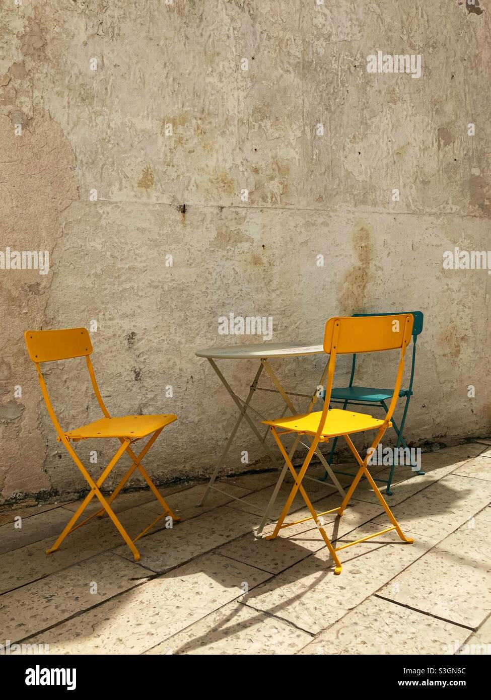 A small bistro table an three Chairs in the Street in Front of a Café in Vieste, Puglia, Italy - Smartphone Captured Stock Image