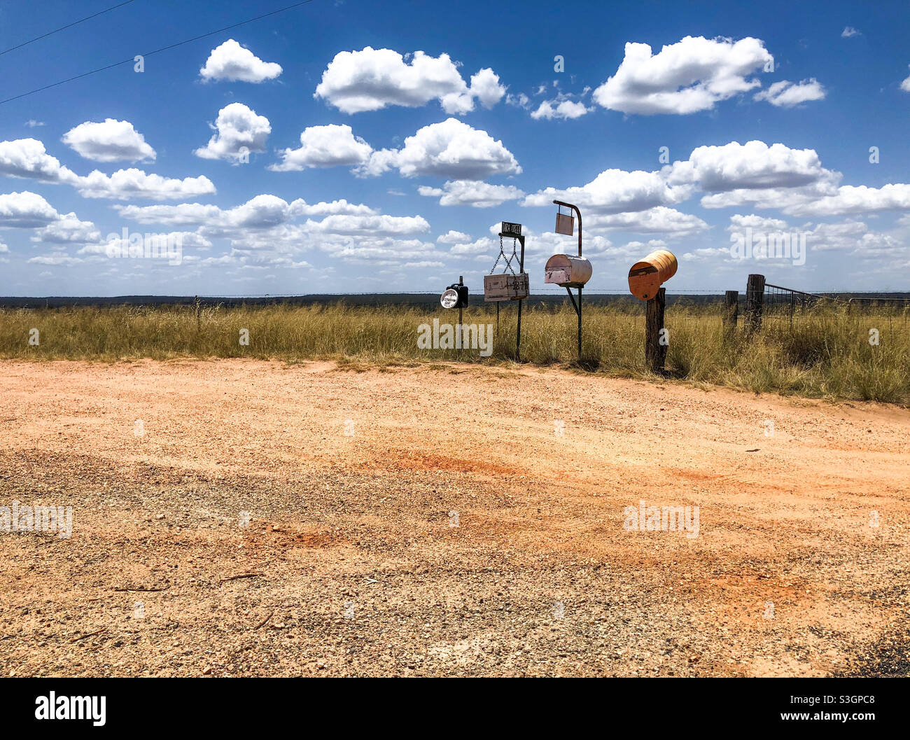 Old Australian letterboxes alongside a dirt road in the countryside under fluffy clouds in a blue sky Stock Photo