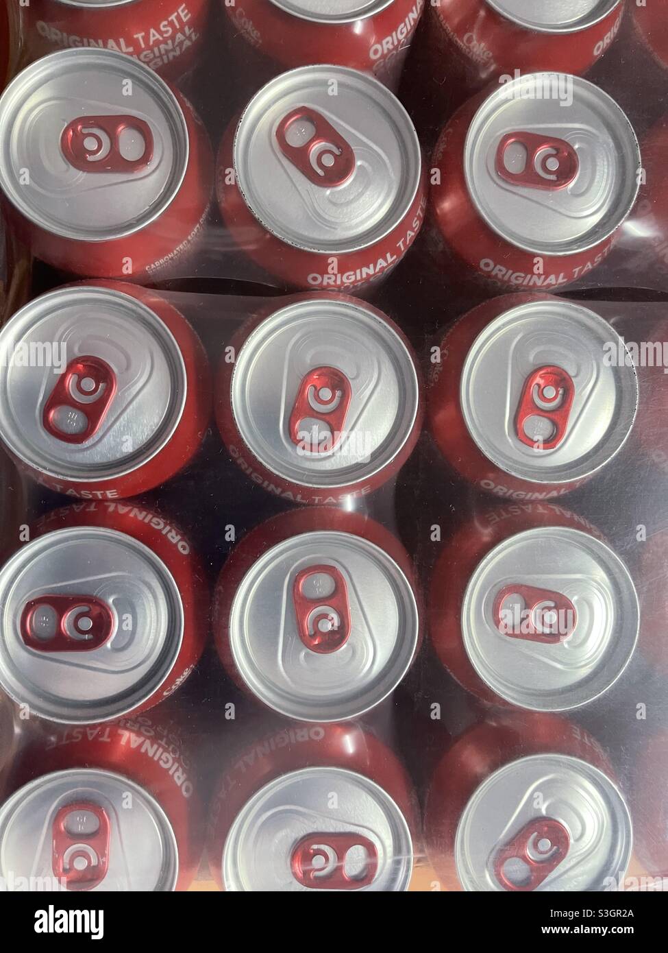 View from top on stowed red tins of softdrink Coca Cola in paper carton and wrapped with transparent plastic cover. Stock Photo