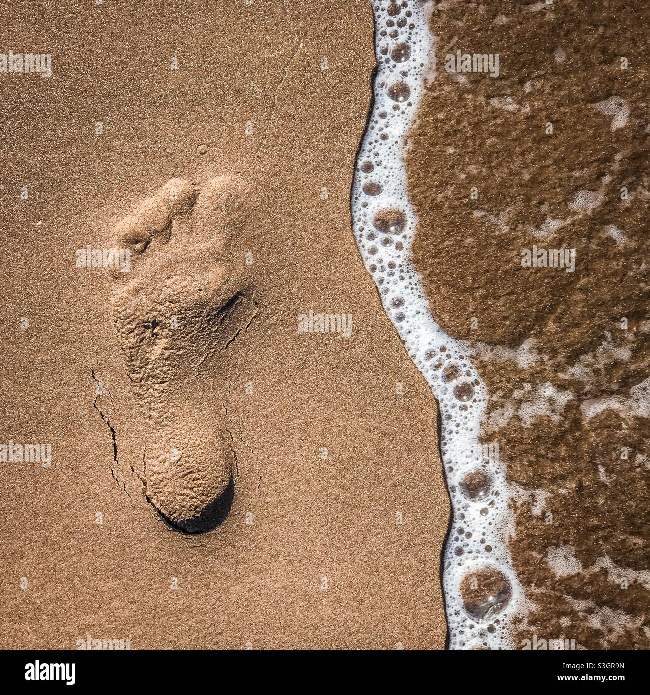 Footprint in sand on a beach being washed away by a wave - Smartphone Captured Stock Image