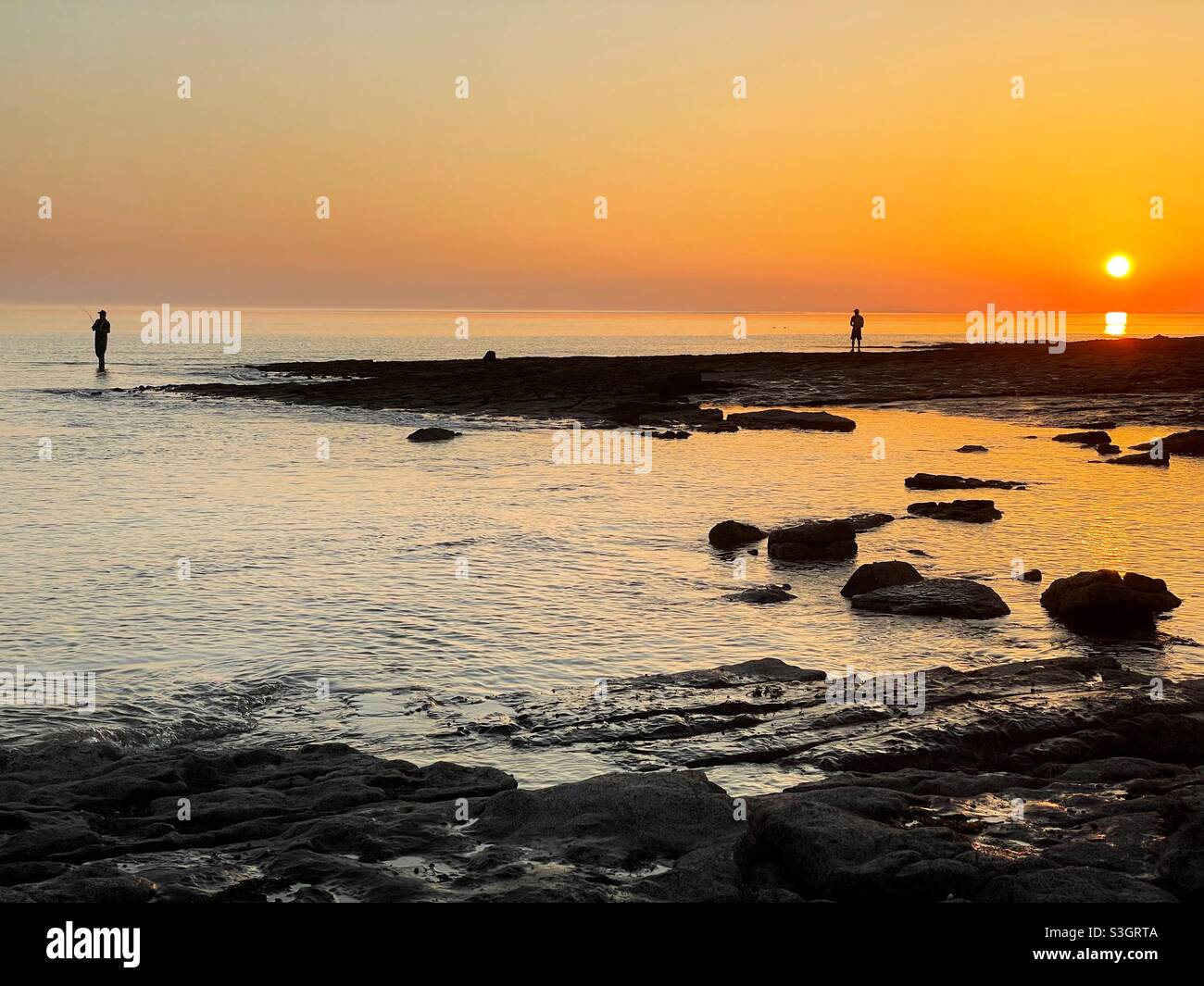 Two anglers silhouetted against the setting sun on the South Wales coast, July. - Smartphone Captured Stock Image