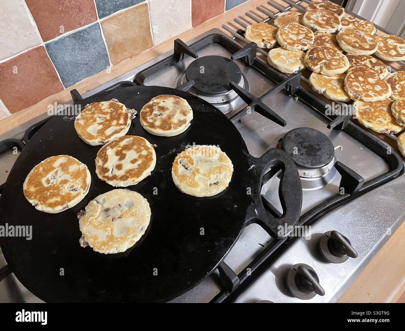 Welsh cakes cooking on a cast iron bake stone next to a pile of