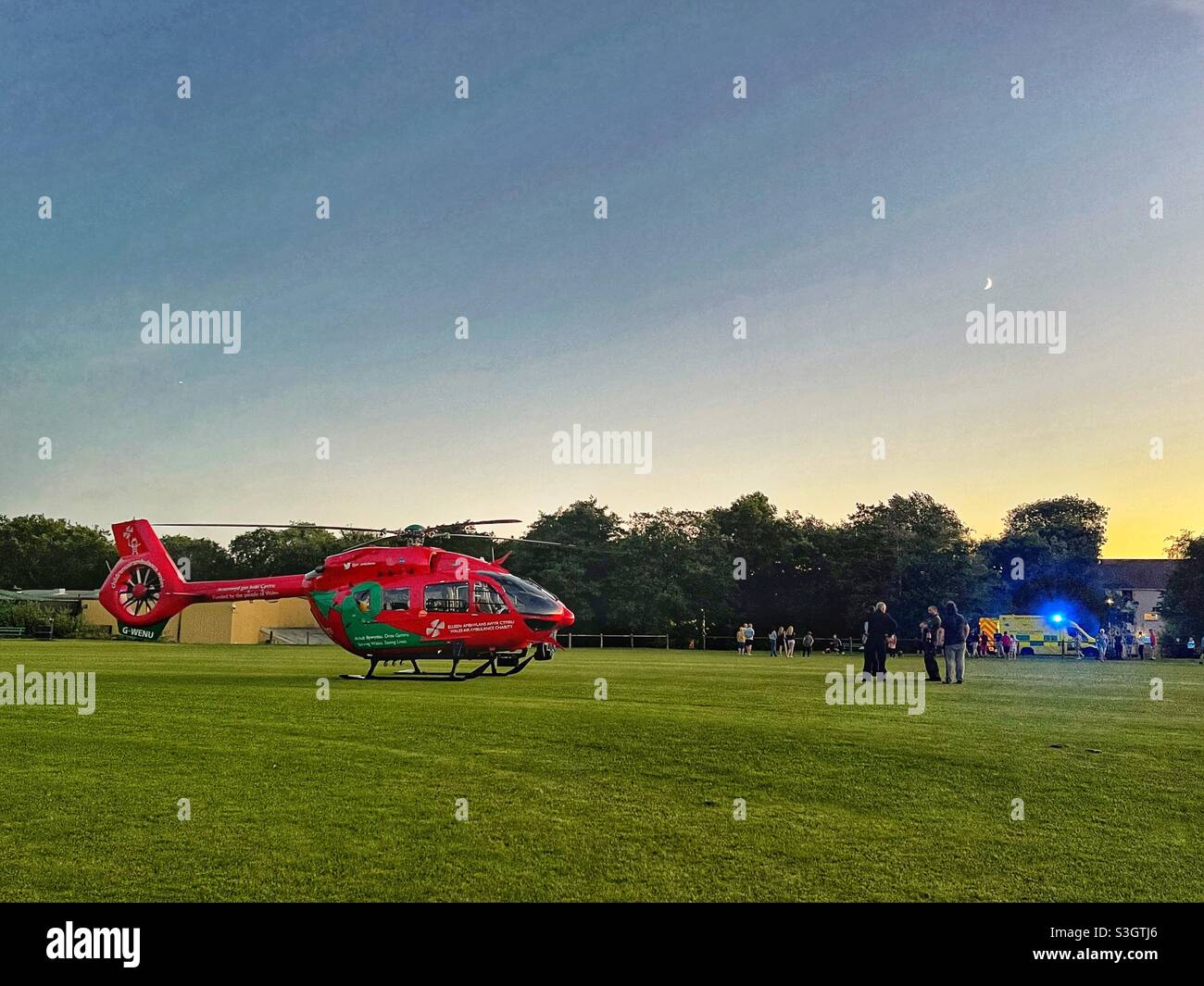 Helicopter of the Wales Air Ambulance service after landing on a cricket pitch to meet the emergency ambulance in the background - Smartphone Captured Stock Image