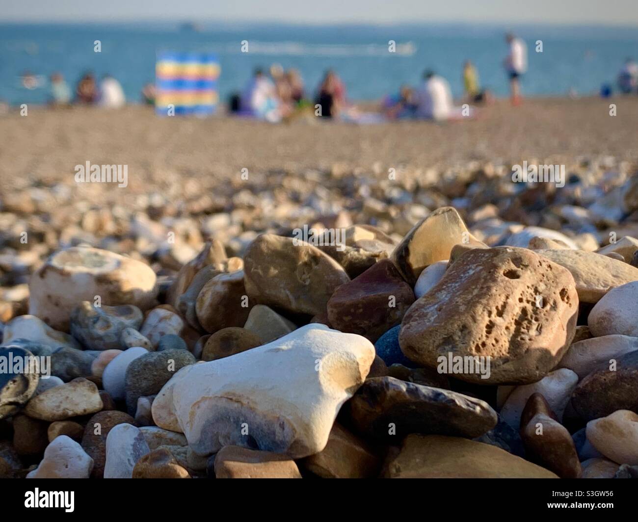 Southsea pebbles on Eastney Beach with holidaying people in the background. - Smartphone Captured Stock Image