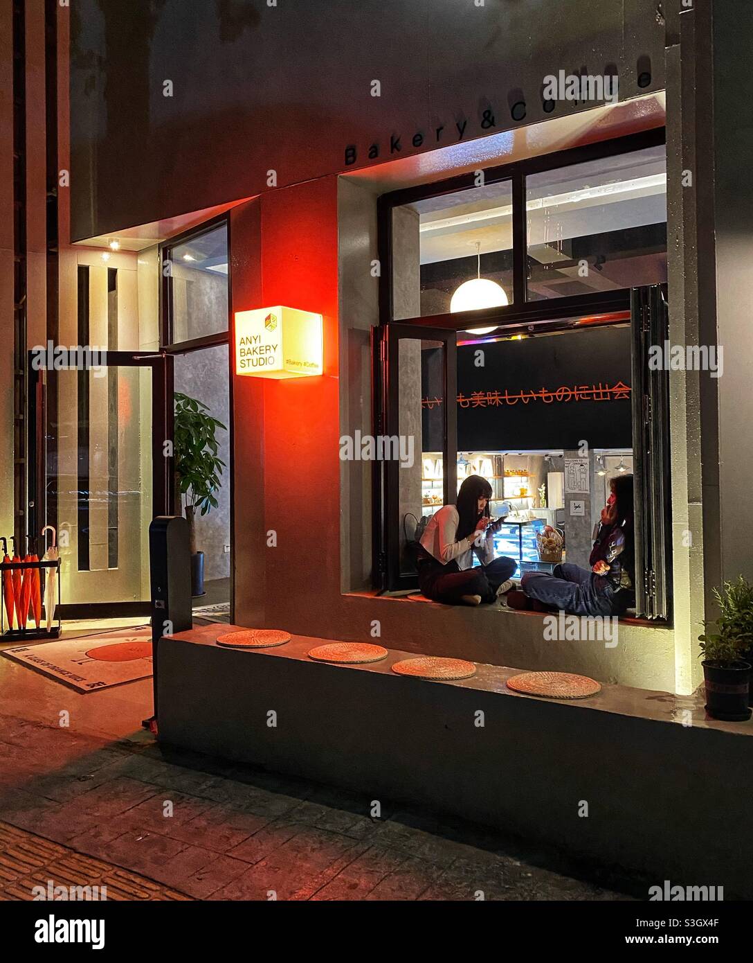 Qingdao, China - May, 2021: night street view of a bakery cafe studio and customers. - Smartphone Captured Stock Image