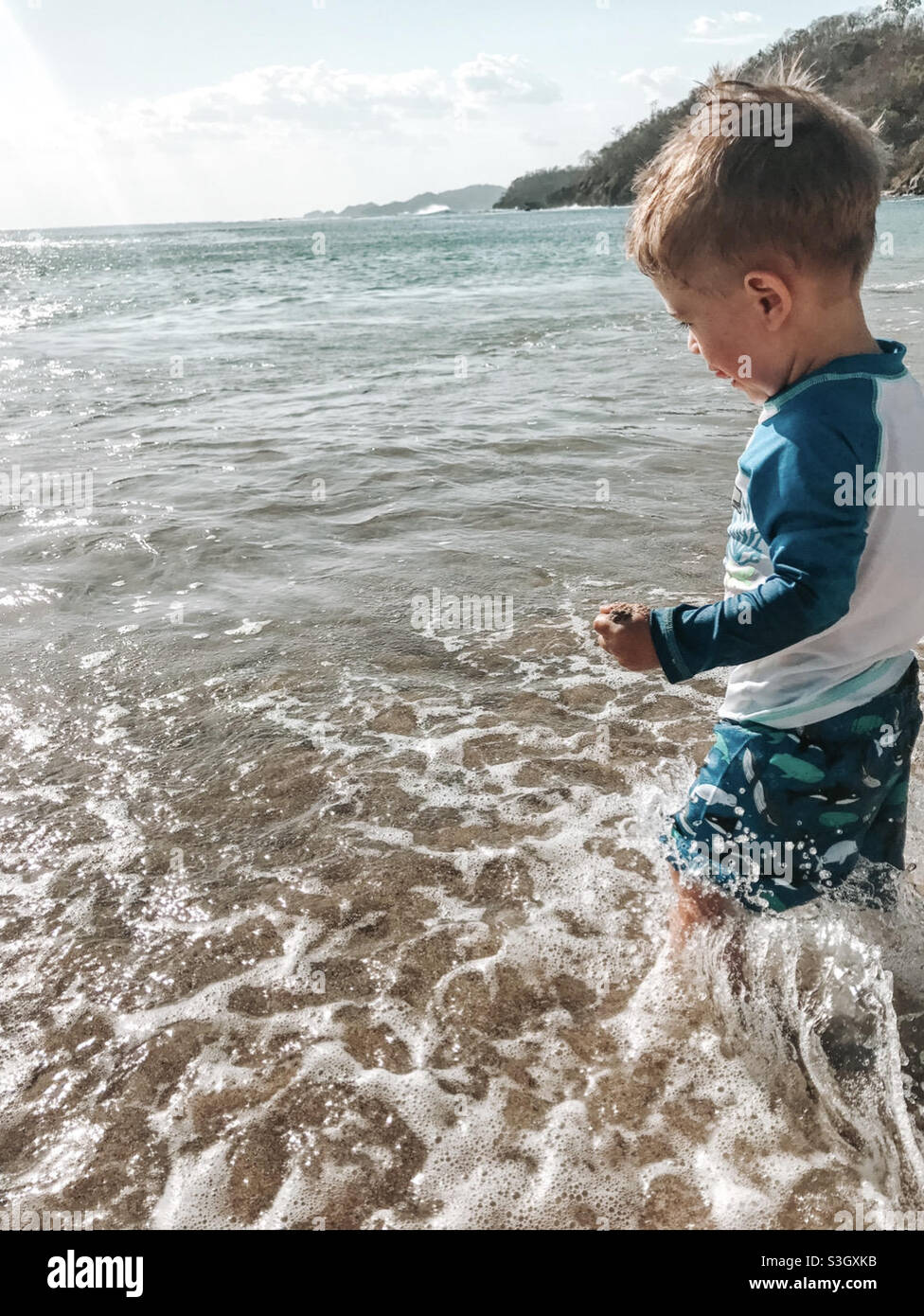 Blonde toddler in the ocean in Nicaragua wearing his whale bathing suit