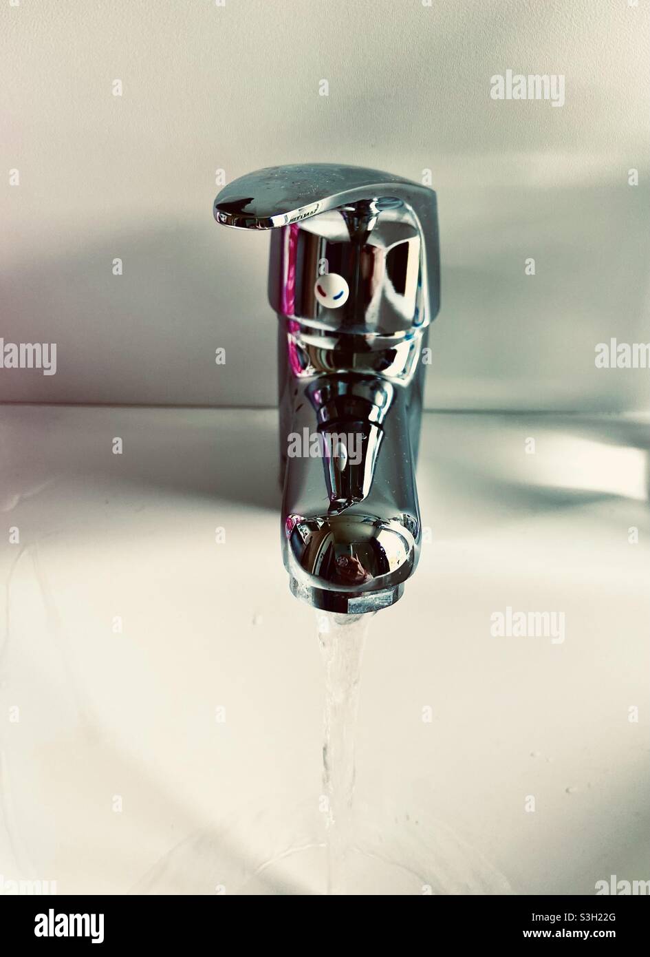Water jet runs from a silver faucet into a white sink Stock Photo