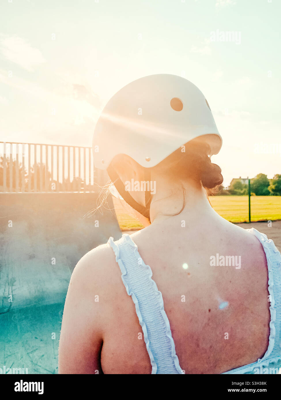 Young woman sitting on top of a half pipe in a skate park at sunset - Smartphone Captured Stock Image