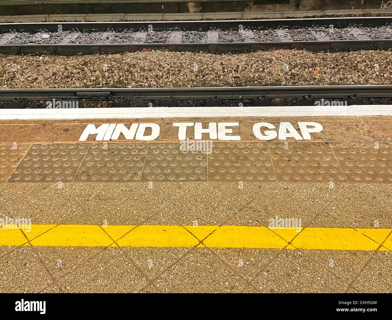 Mind the Gap sign on the edge of a railway station platform with the track in the background Stock Photo