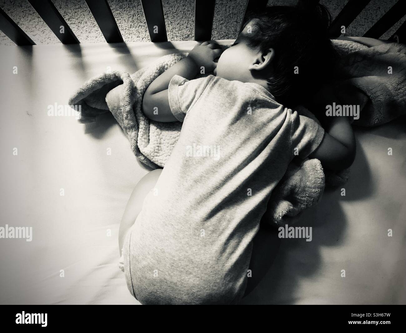 Tummy sleeping baby boy sucking his thumb in a crib in black and white Stock Photo