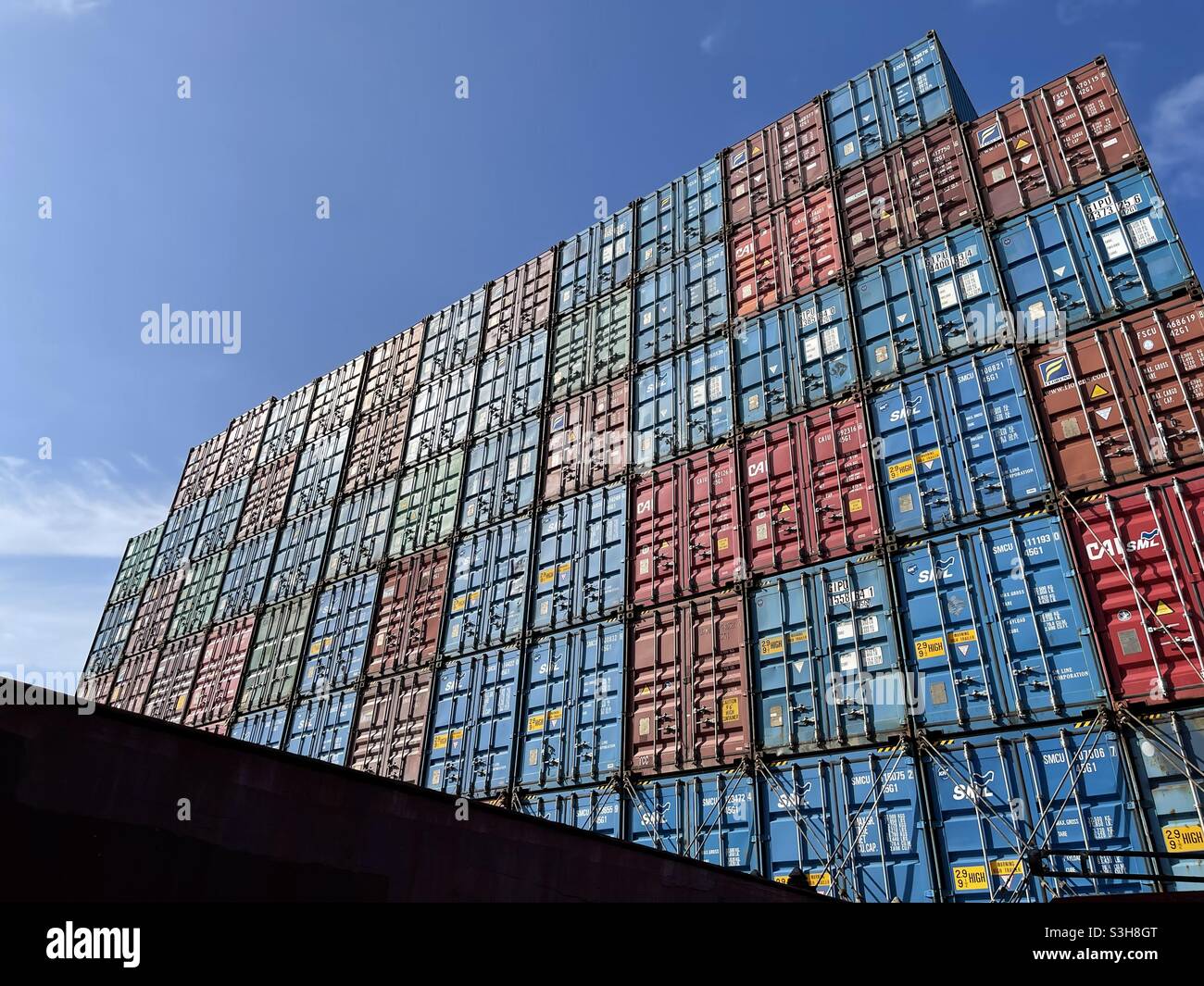 Stowed containers and secured containers with lashing bars and twist locks on the merchant container vessel during sunny summertime underway through ocean under blue sky. Stock Photo