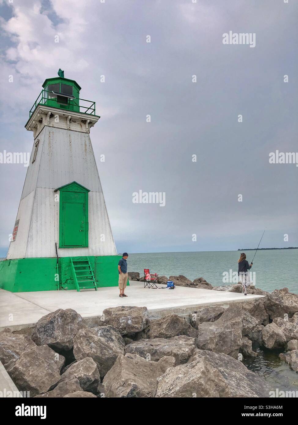 Two people standing on a pier next to a lighthouse. - Smartphone Captured Stock Image