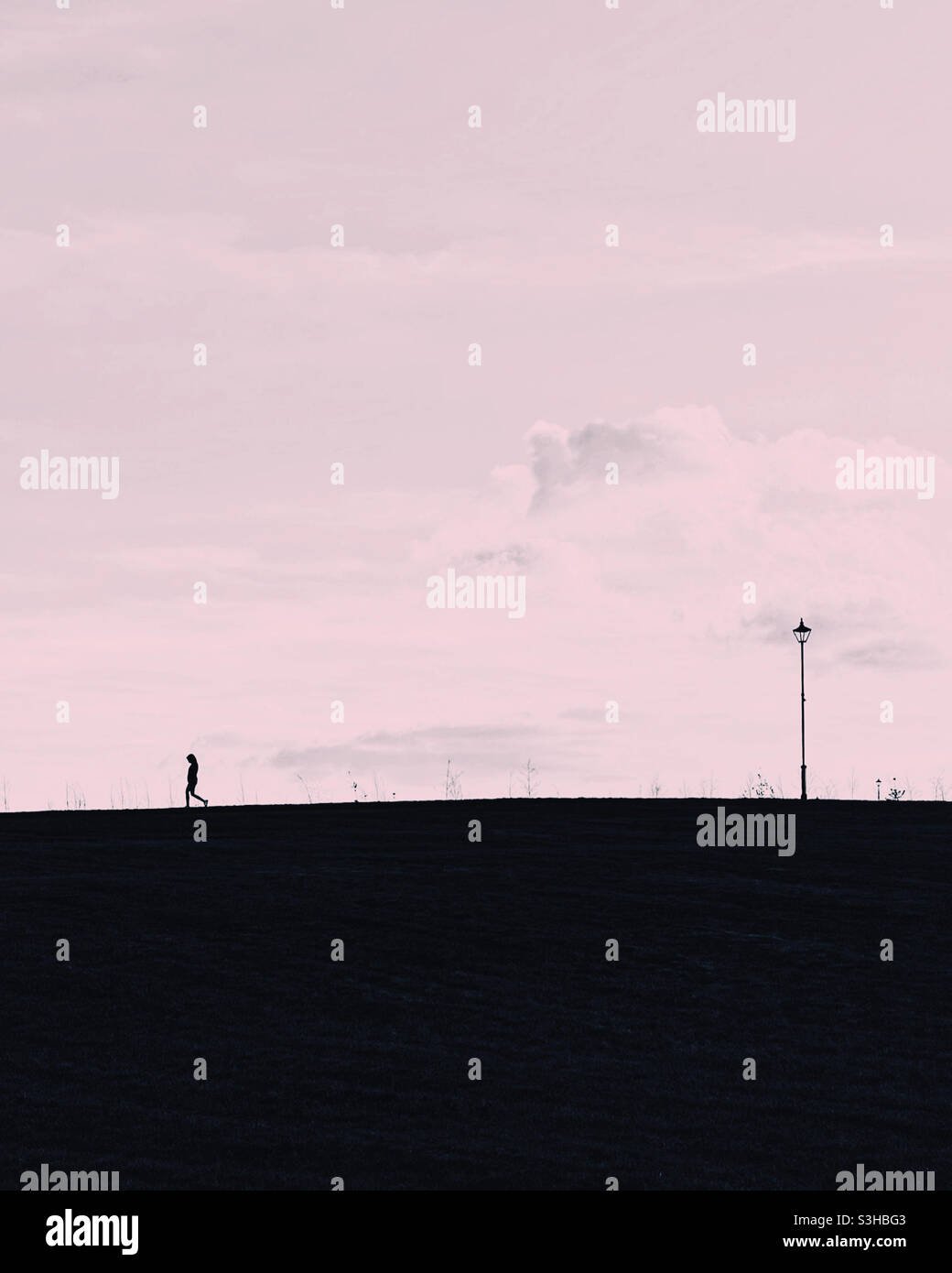 Lone silhouette on hill with lamppost. Stock Photo