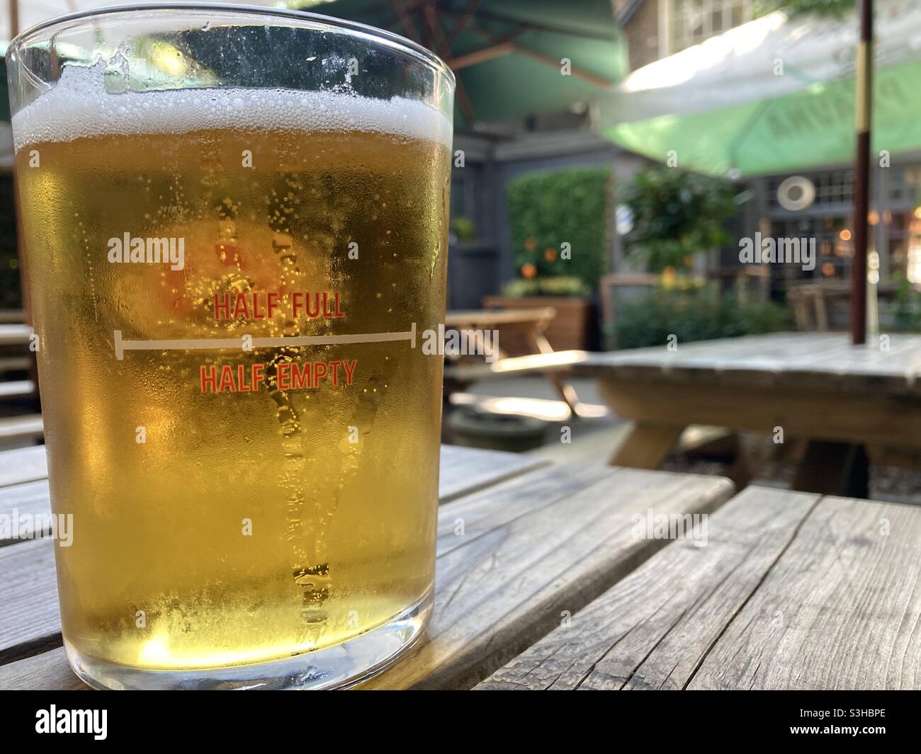 Pint glass full of beer with a half full & half empty indicator on a pub beer garden table. Stock Photo