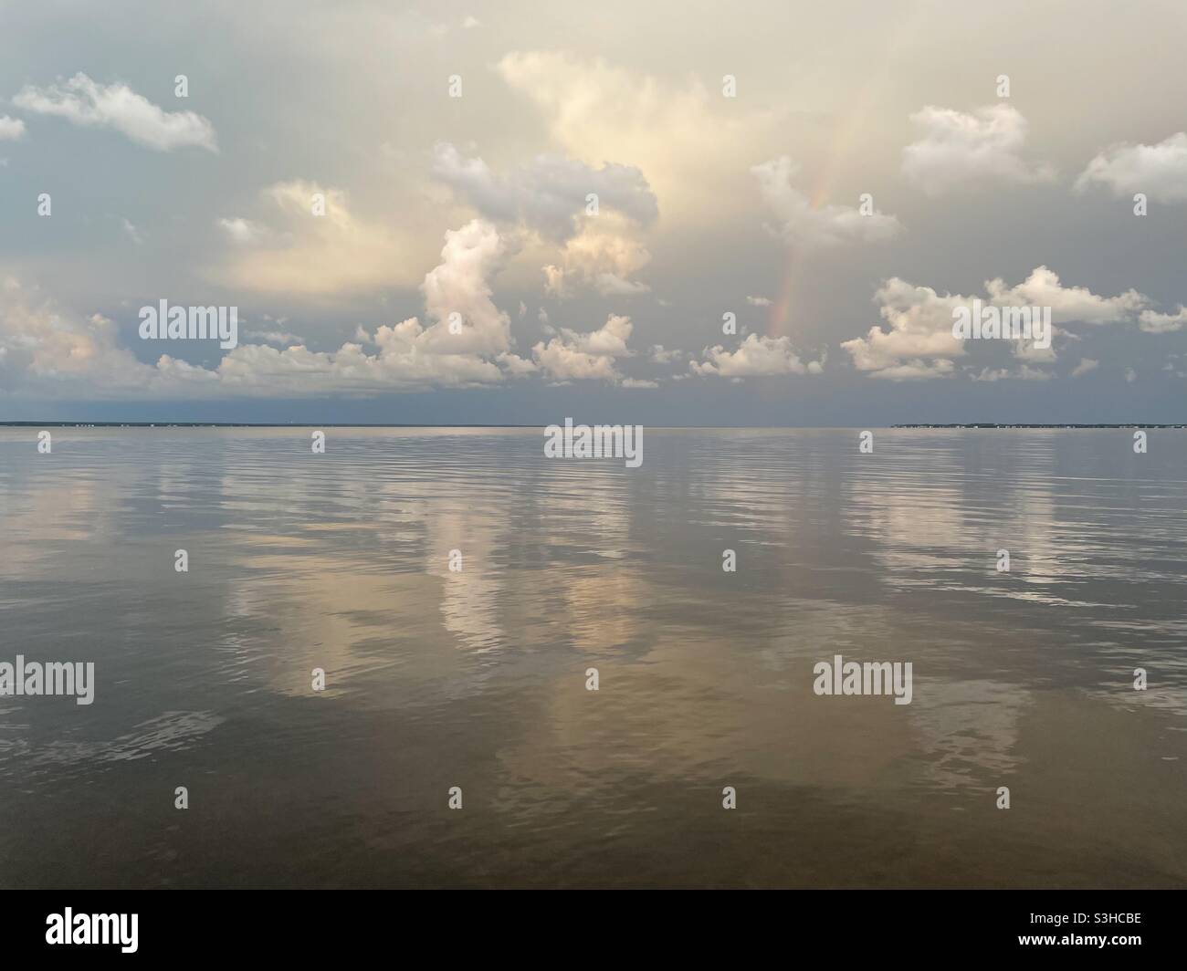 Sunset clouds with a rainbow reflecting onto bay water Stock Photo - Alamy