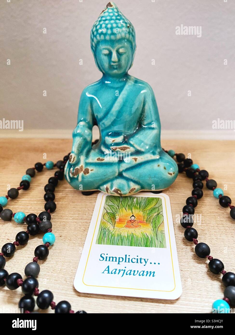 A Buddha figurine, prayer beads, and upturned dharma card with word 'simplicity'. Stock Photo