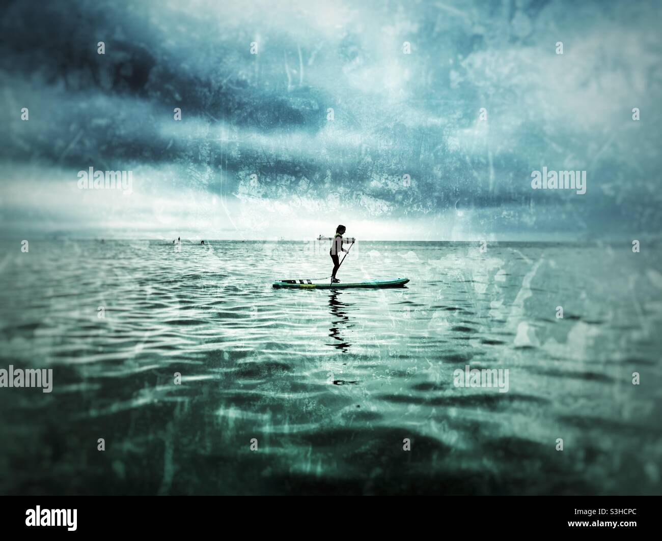 Young woman SUP boarding on the ocean. Boat in the distance. Stock Photo