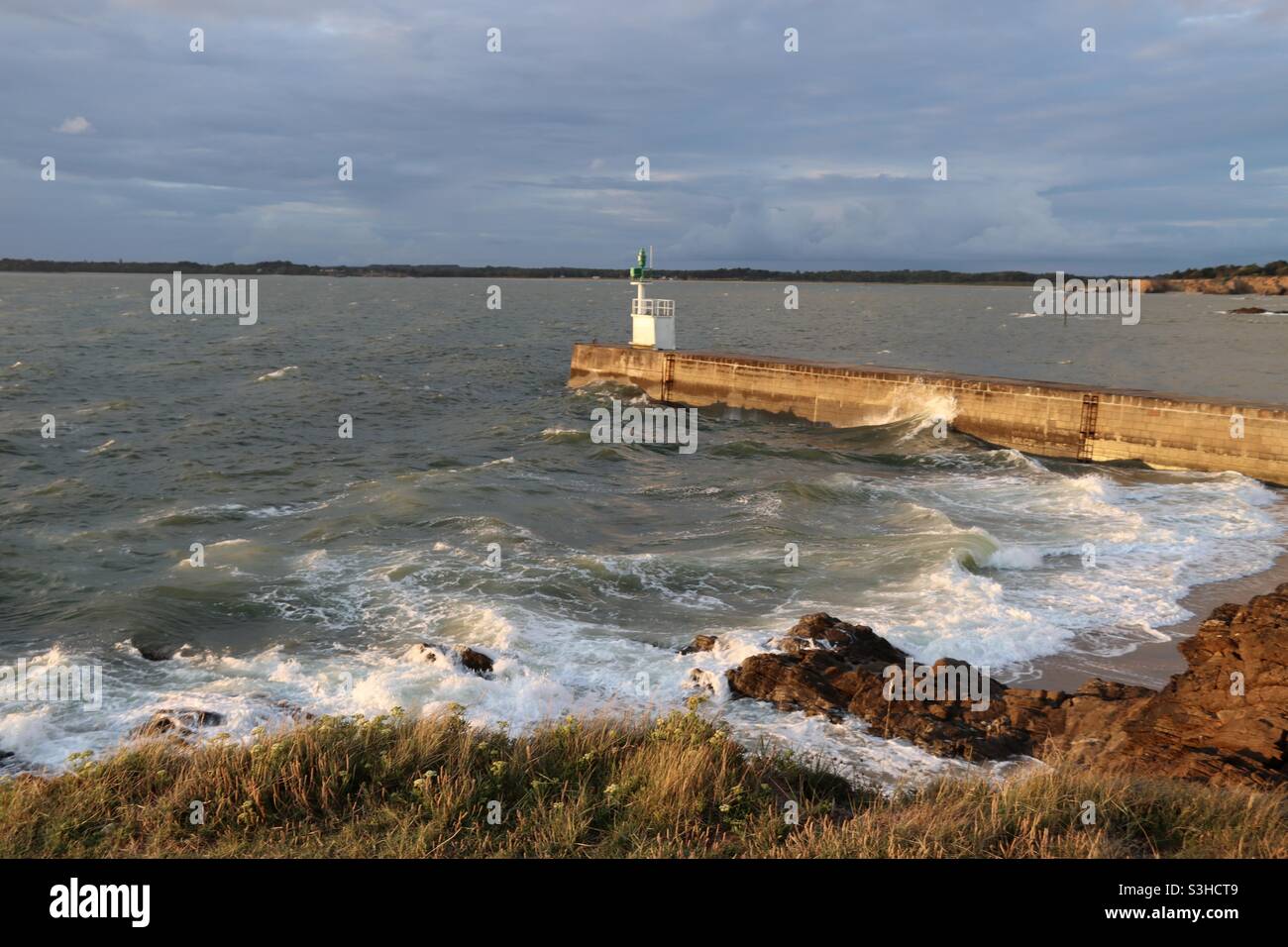 Waves splashing on the pier at sunset time in Merquel peninsula Loire Atlantique, France - Smartphone Captured Stock Image